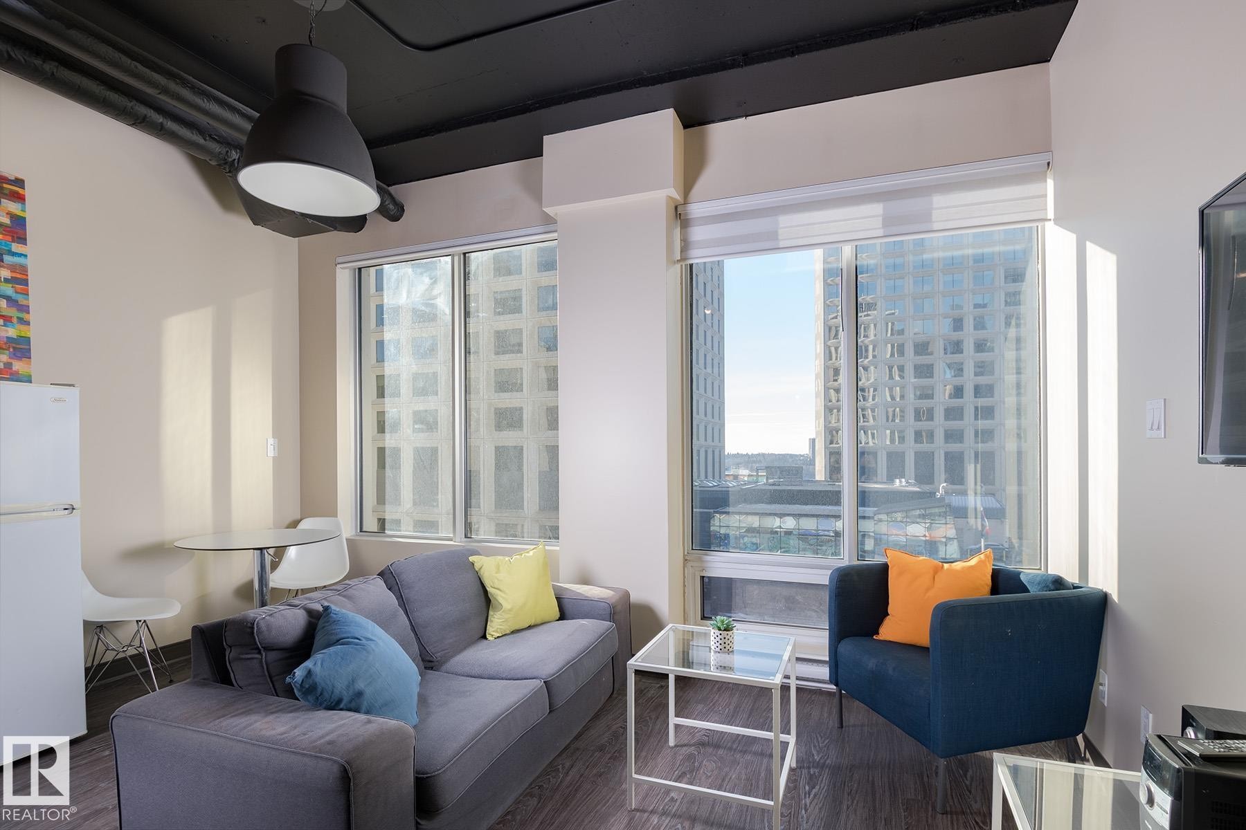 Floor-to-ceiling windows with roller shades, wood-finish flooring, and industrial-style exposed ceiling pipes - 411 10024 Jasper Avenue, Edmonton, AB
