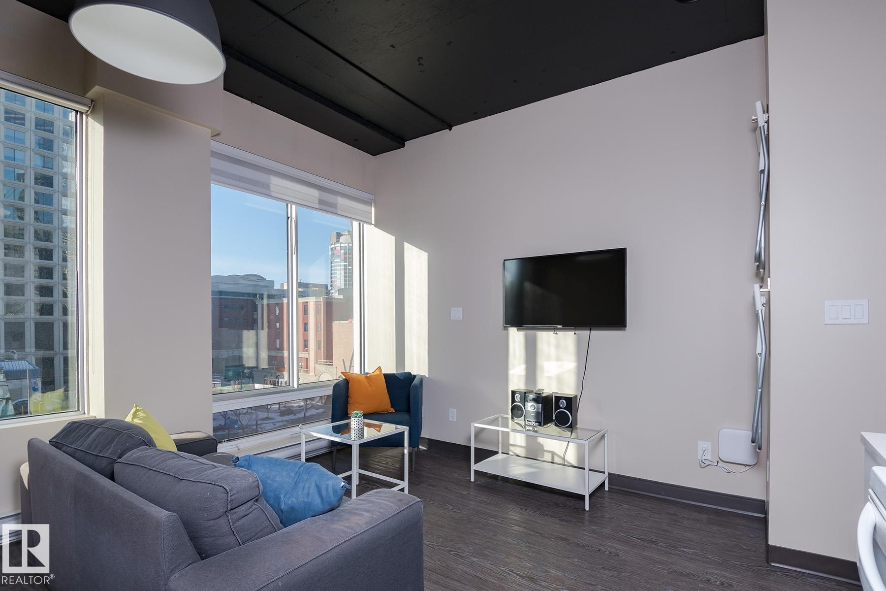 Expansive windows with roller shades, dark wood-finish flooring, and a black ceiling create a contemporary aesthetic - 411 10024 Jasper Avenue, Edmonton, AB