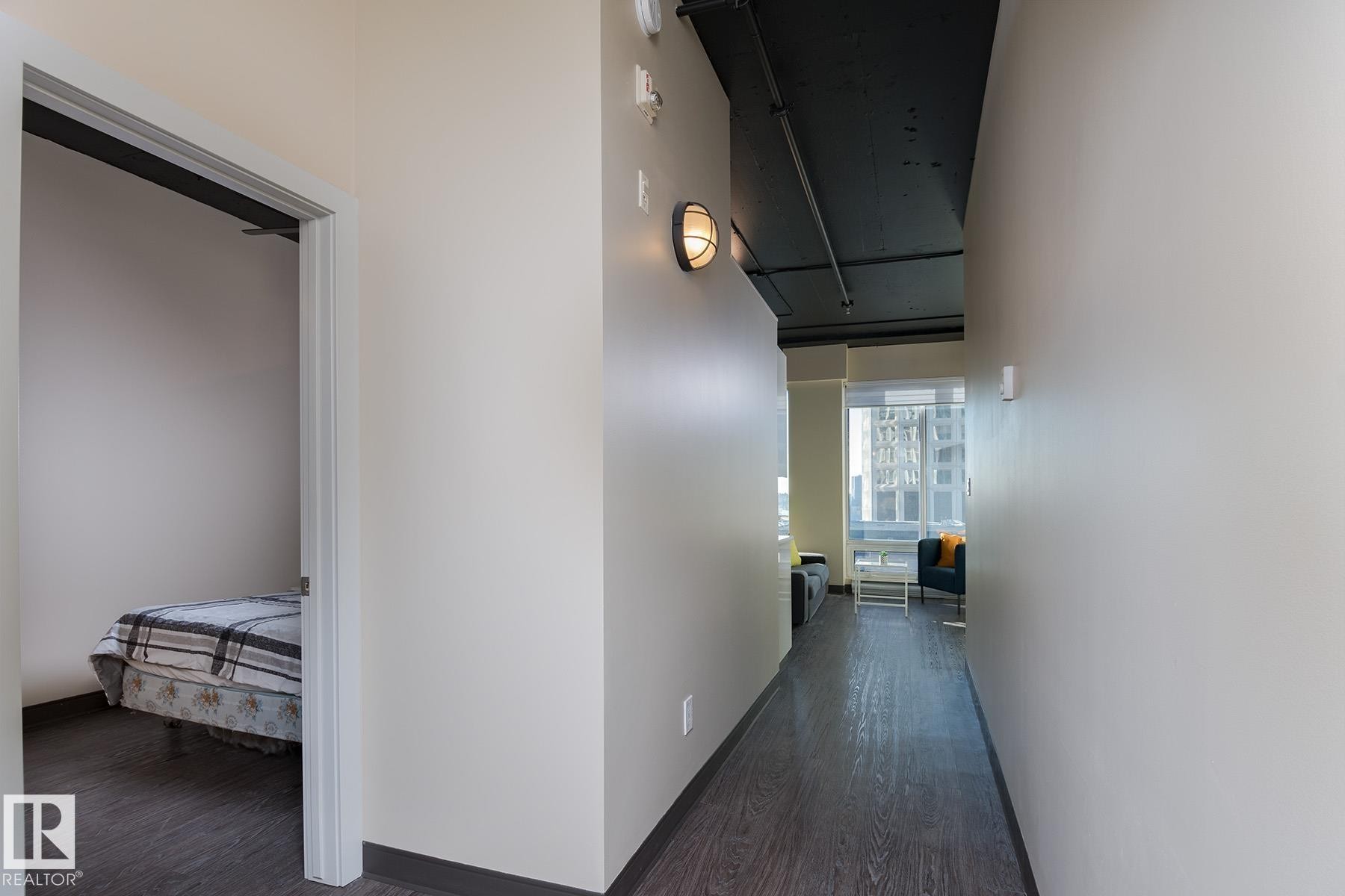 Hallway featuring wood-finish flooring, light-toned walls, and industrial-style wall sconces - 411 10024 Jasper Avenue, Edmonton, AB