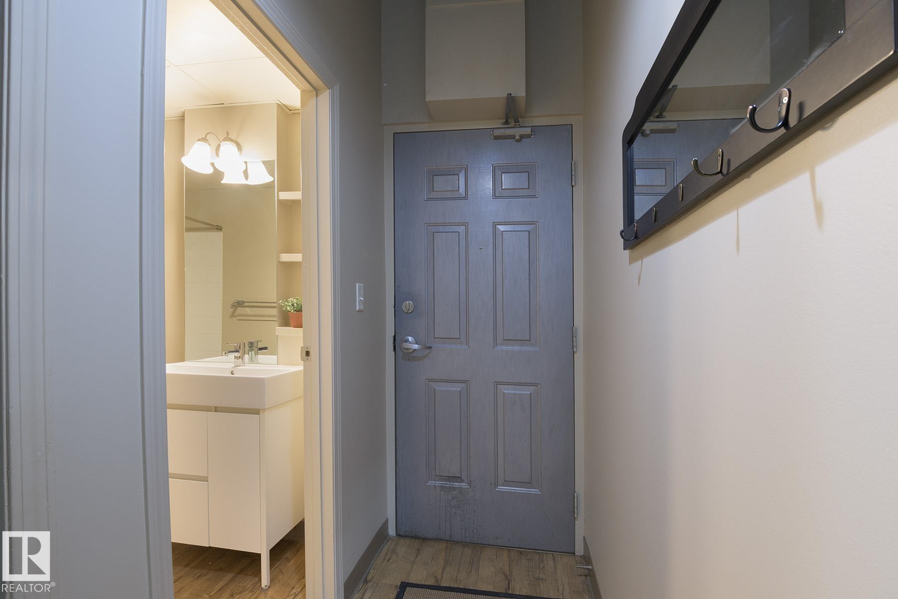 Entryway featuring wood-finish flooring and a wall-mounted coat rack with mirror - #412 10024 Jasper Av Nw, Edmonton, AB - Indoor Photo Showing Other Room