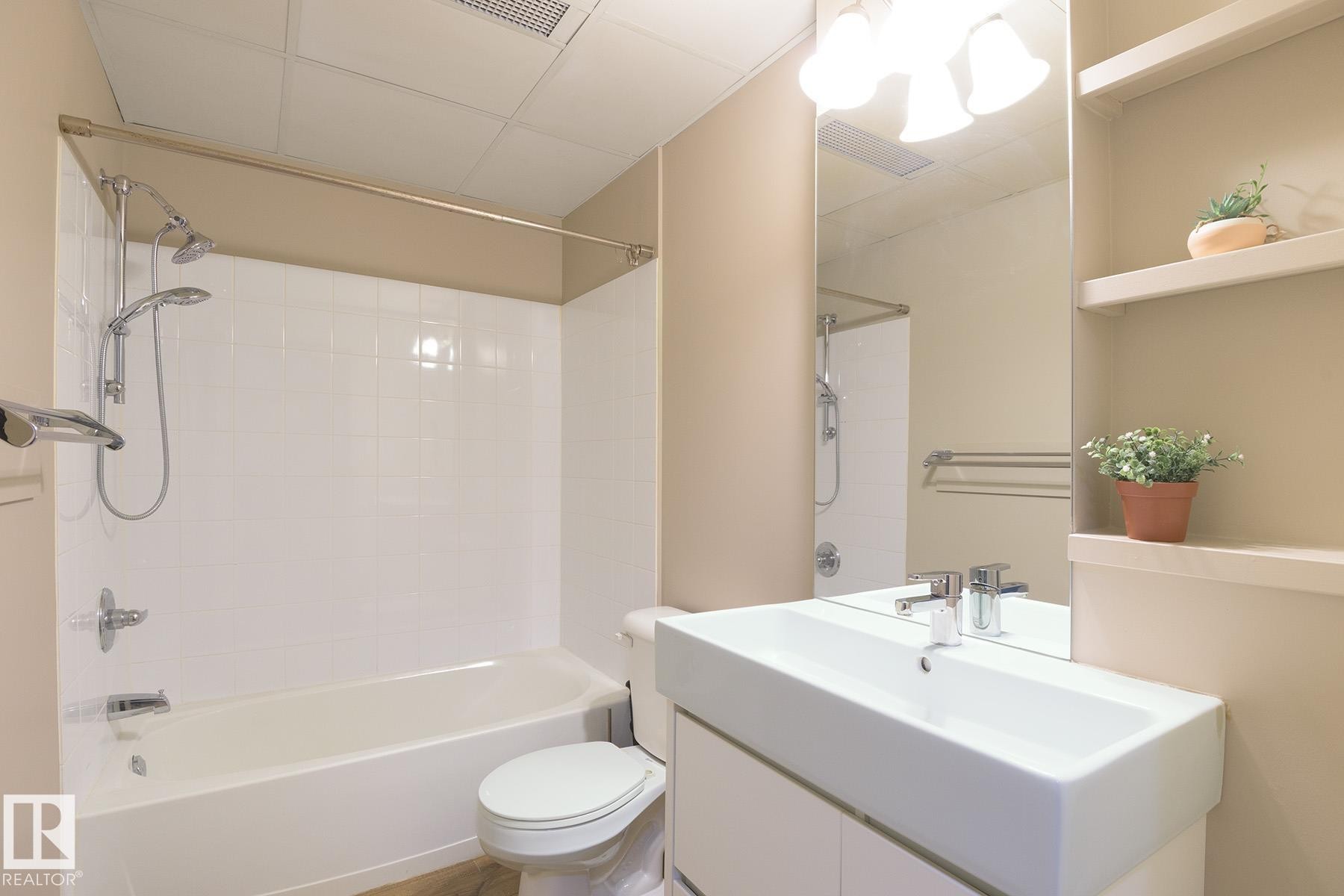 Bathroom featuring a white bathtub with subway tile surround, chrome fixtures, and a dual showerhead system - #412 10024 Jasper Av Nw, Edmonton, AB - Indoor Photo Showing Bathroom