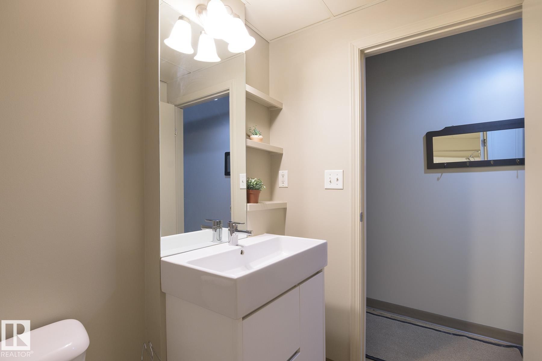 Bathroom featuring a modern white vanity with an integrated rectangular sink, a polished chrome single-handle faucet, a large wall-mounted mirror, and a three-light vanity fixture - #412 10024 Jasper Av Nw, Edmonton, AB - Indoor Photo Showing Bathroom