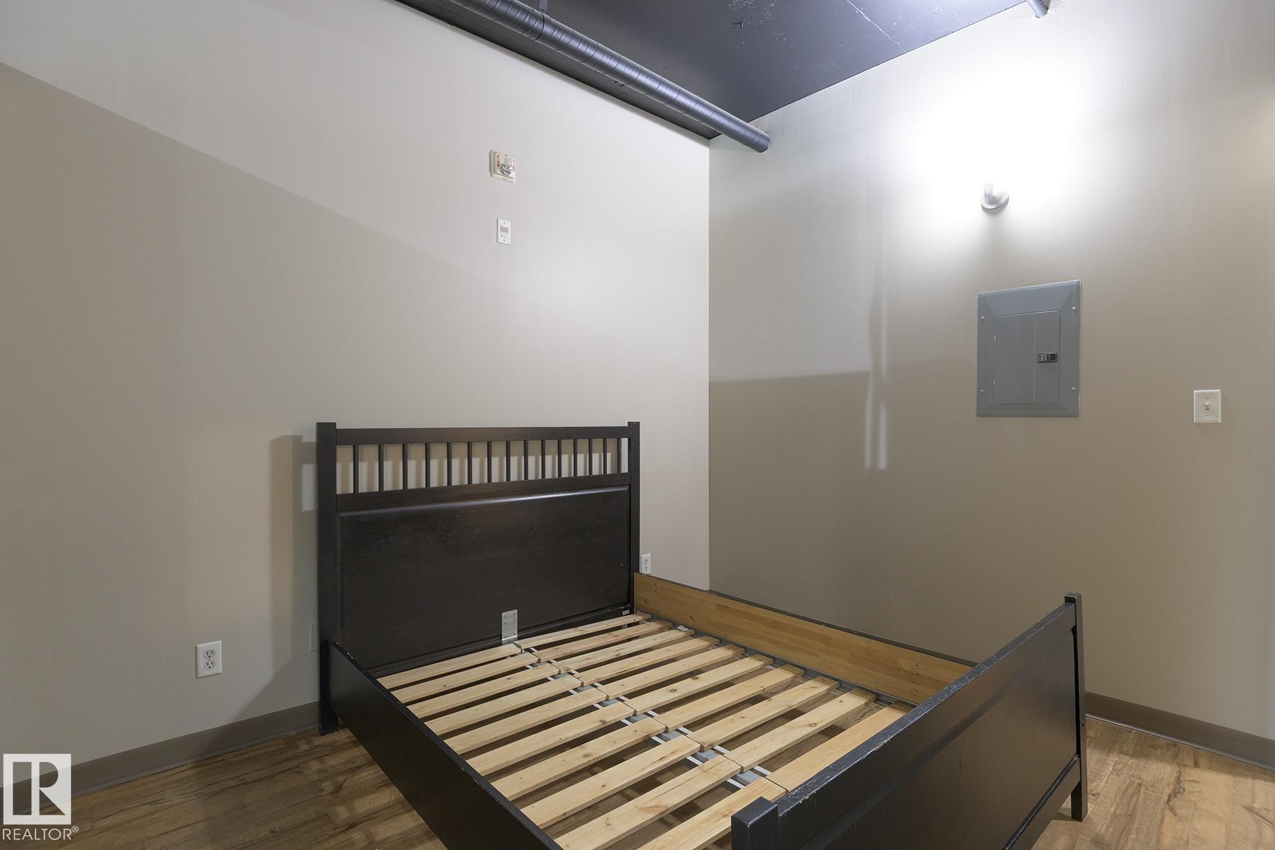 Spacious room featuring wood-finish flooring, light neutral wall paint, and exposed overhead ductwork - #412 10024 Jasper Av Nw, Edmonton, AB - Indoor Photo Showing Bedroom