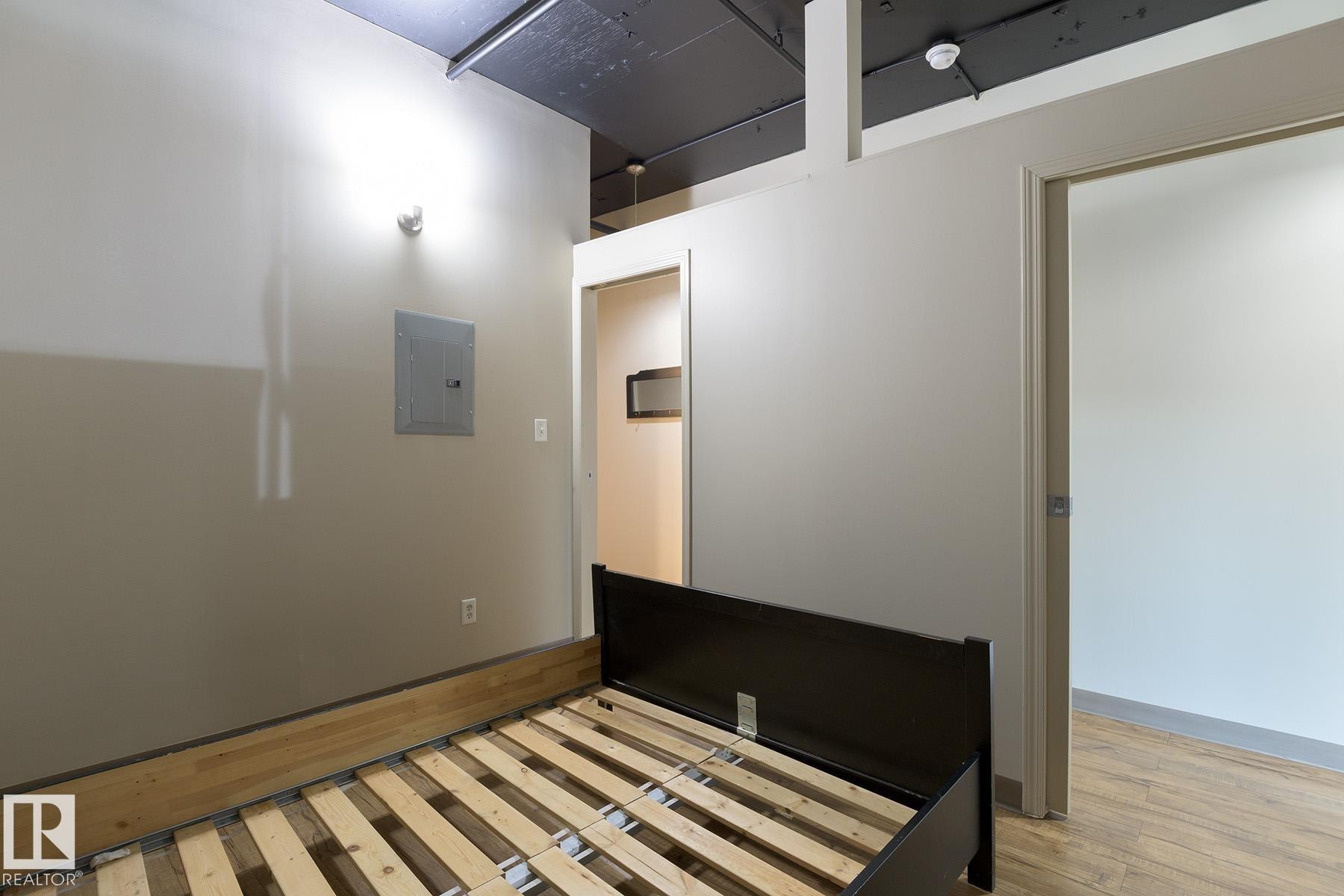 Interior space featuring wood-finish flooring, exposed ceiling elements, and a partial wall with a doorway - #412 10024 Jasper Av Nw, Edmonton, AB - Indoor