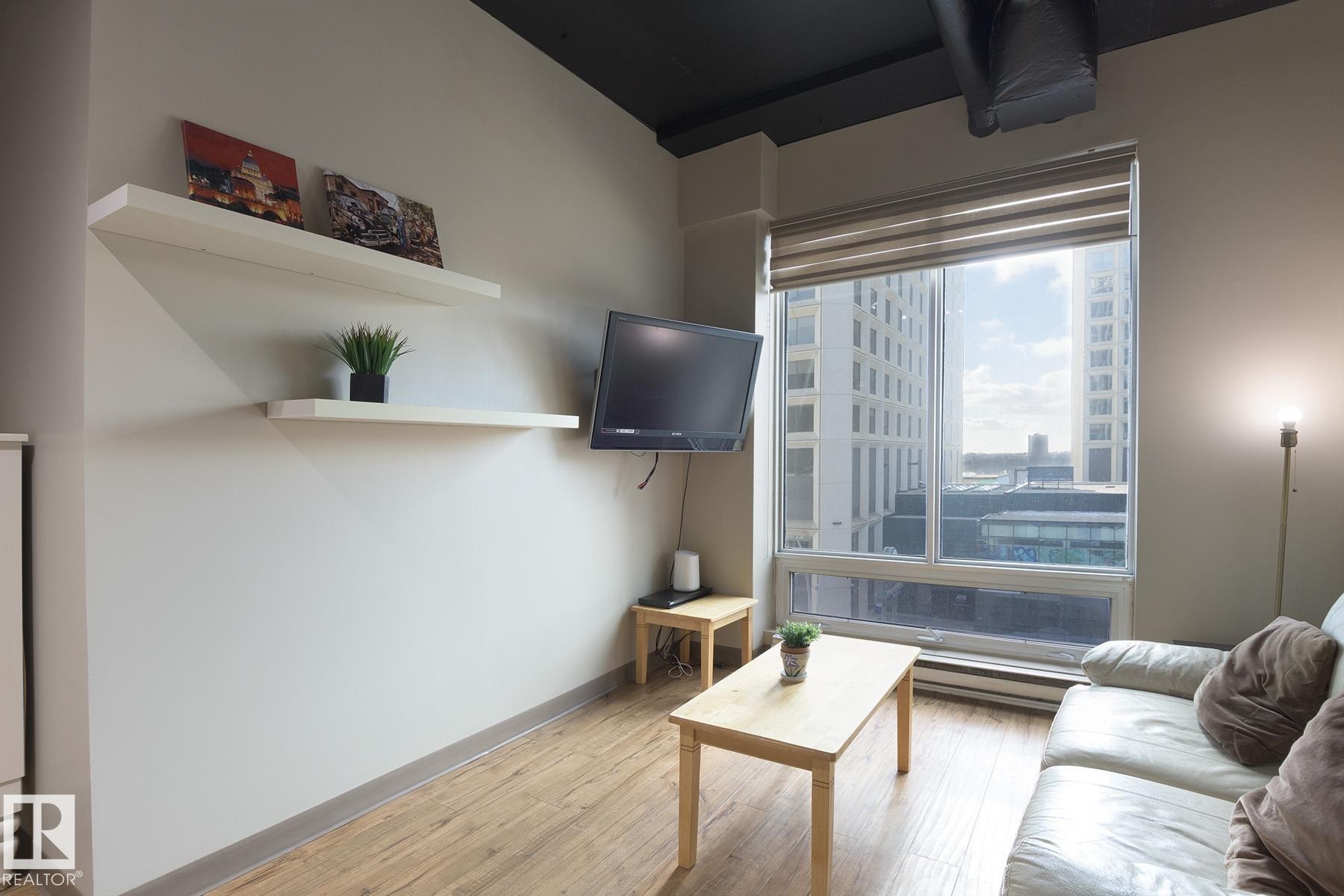 Living area featuring a large window with roller shades, wood-finish flooring, and a dark-painted ceiling - #412 10024 Jasper Av Nw, Edmonton, AB - Indoor