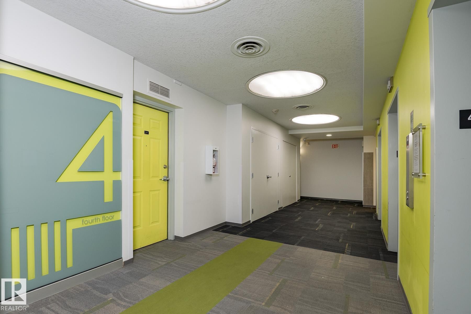 Modern hallway featuring recessed circular lighting, contrasting gray and bright yellow wall finishes, and patterned carpet flooring with a green accent strip - #412 10024 Jasper Av Nw, Edmonton, AB - Indoor Photo Showing Other Room