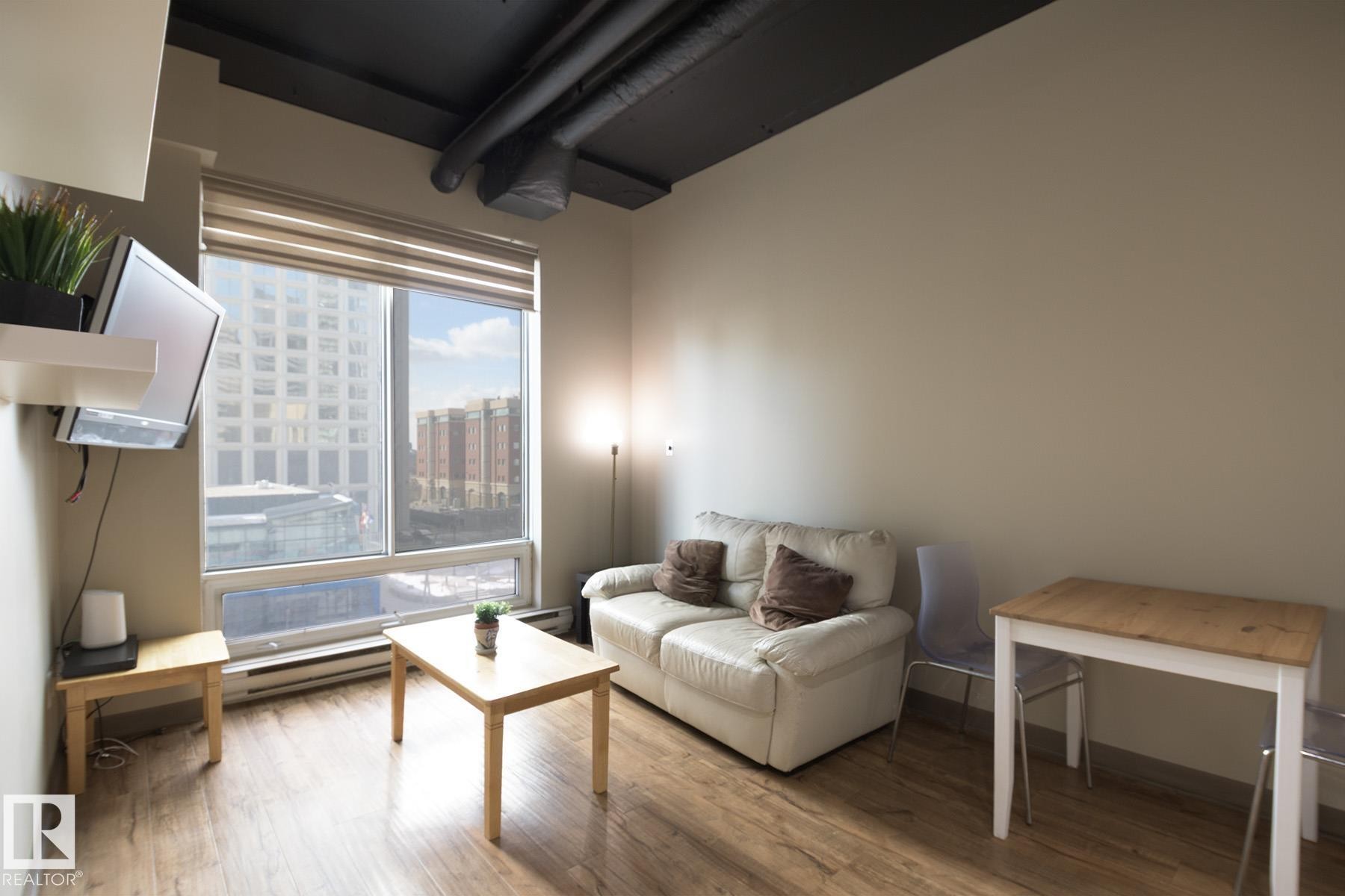Living space featuring wood-finish flooring and a large window with roller shades - #412 10024 Jasper Av Nw, Edmonton, AB - Indoor Photo Showing Living Room