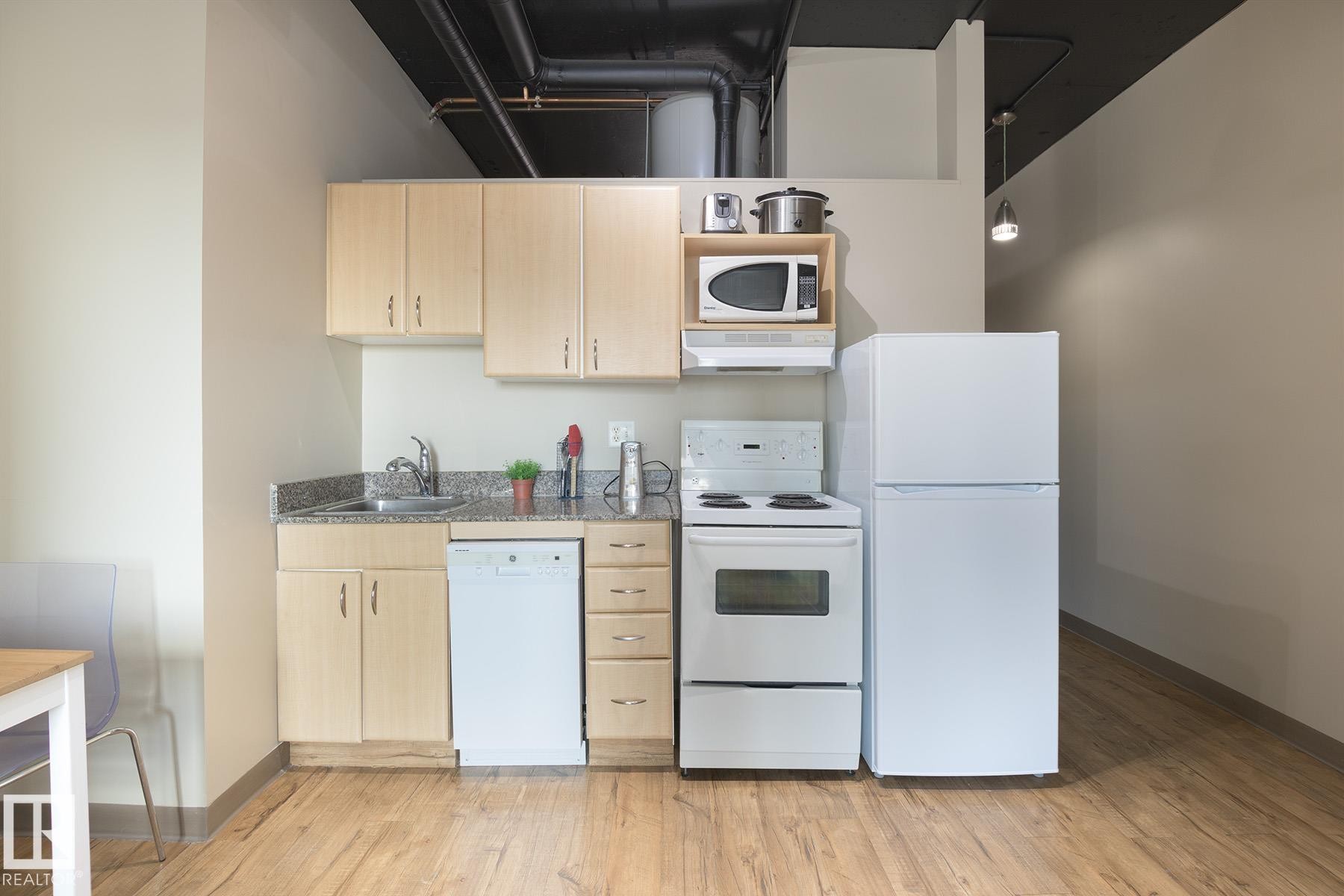 Kitchenette featuring wood-finish flooring, light-toned cabinetry, a granite-patterned countertop, white appliances, and exposed ductwork - #412 10024 Jasper Av Nw, Edmonton, AB - Indoor Photo Showing Kitchen