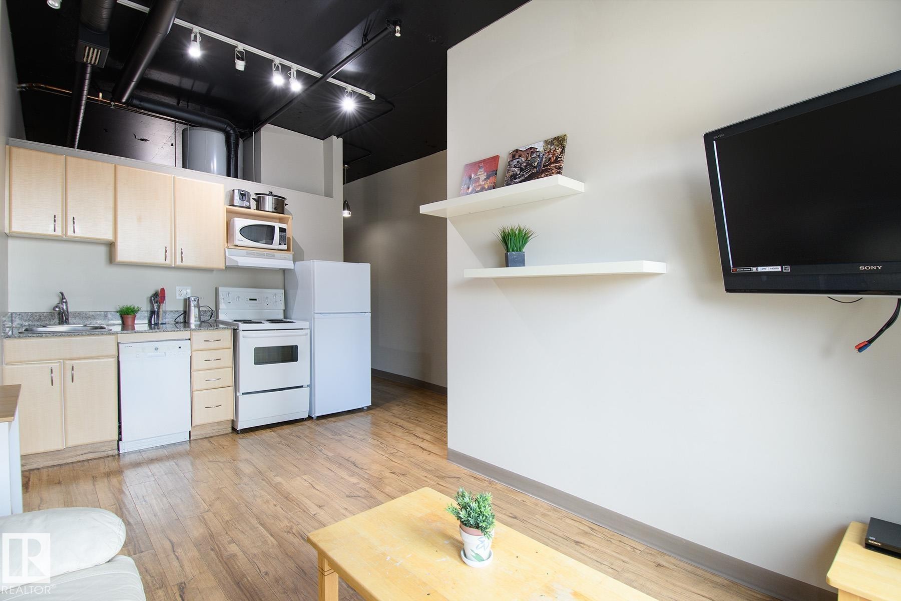 Kitchen area featuring wood-finish flooring, light cabinetry, a white dishwasher, a white electric range, and a white refrigerator - #412 10024 Jasper Av Nw, Edmonton, AB - Indoor Photo Showing Kitchen