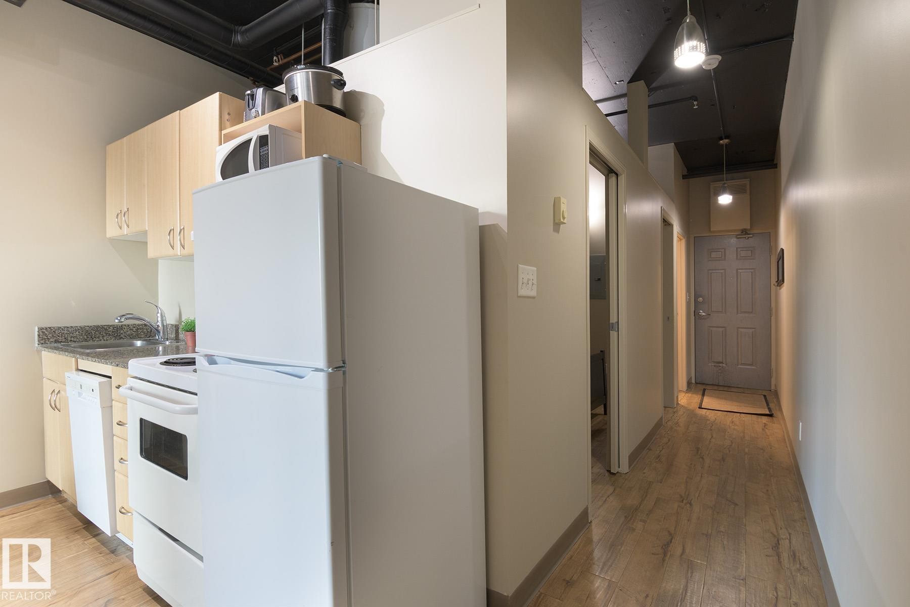 Compact kitchen featuring wood-finish cabinetry, granite-style countertops, and full-size appliances - #412 10024 Jasper Av Nw, Edmonton, AB - Indoor Photo Showing Kitchen