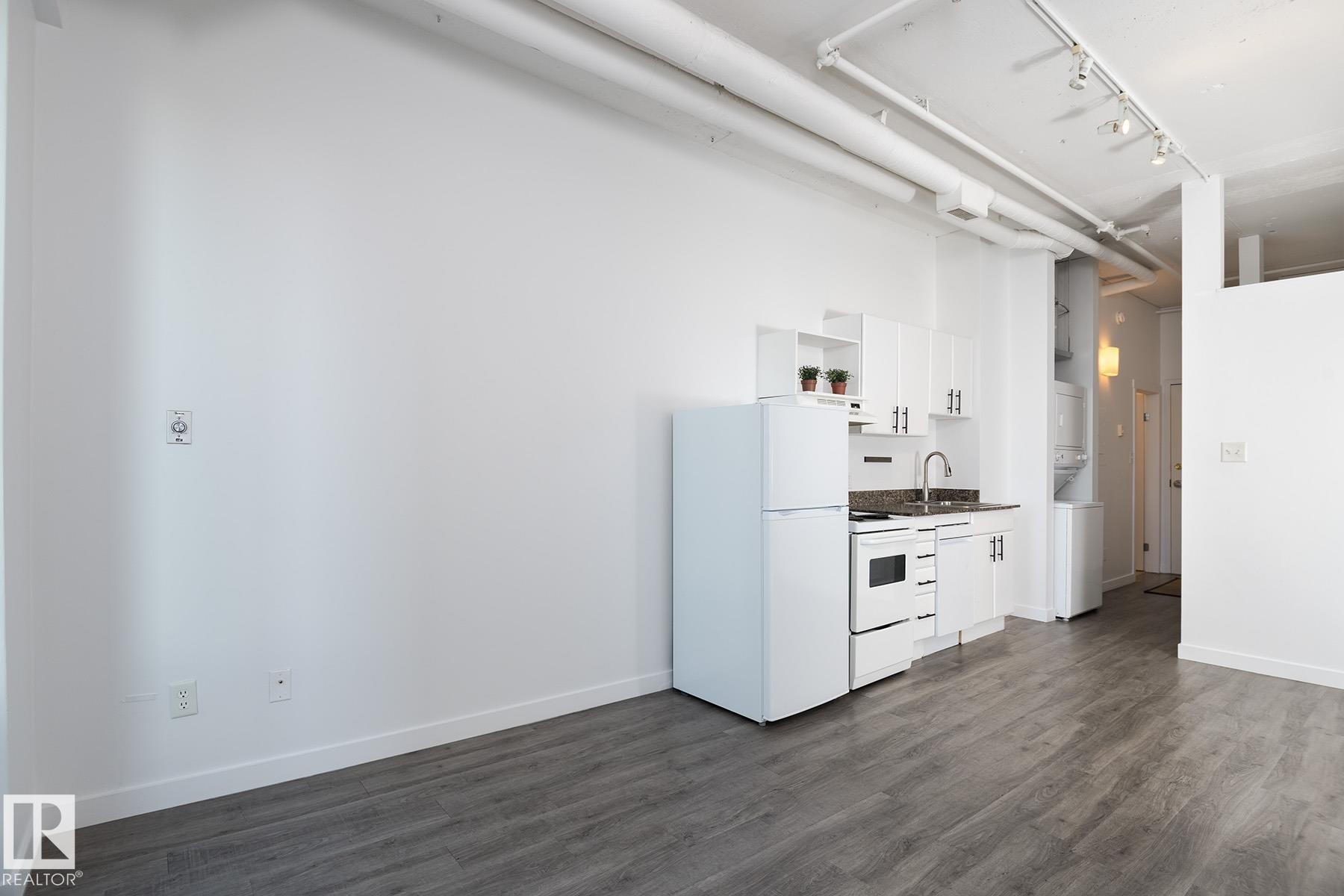 Compact kitchen featuring white appliances, white cabinetry with dark hardware, and a stone-finish countertop - 910 10024 Jasper Avenue, Edmonton, AB
