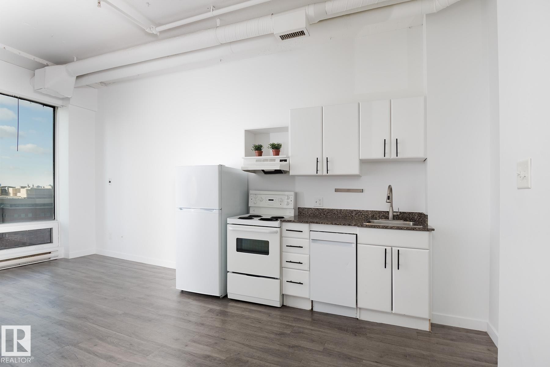 Compact kitchen area featuring white cabinetry, a dishwasher, a full-size refrigerator, and a range with overhead ventilation - 910 10024 Jasper Avenue, Edmonton, AB