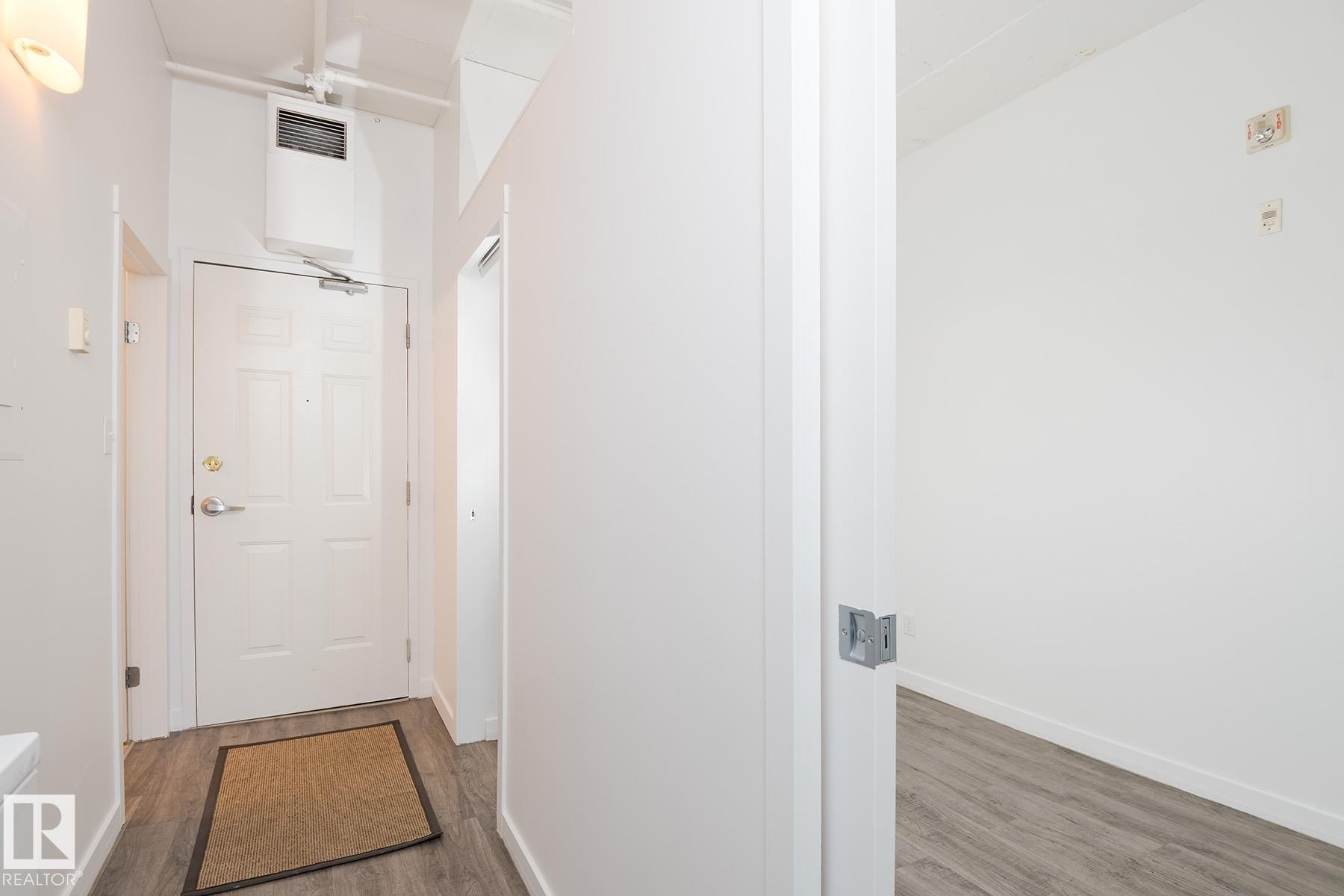 Entryway featuring a paneled door with polished hardware, wood-finish flooring, and crisp white walls - 910 10024 Jasper Avenue, Edmonton, AB