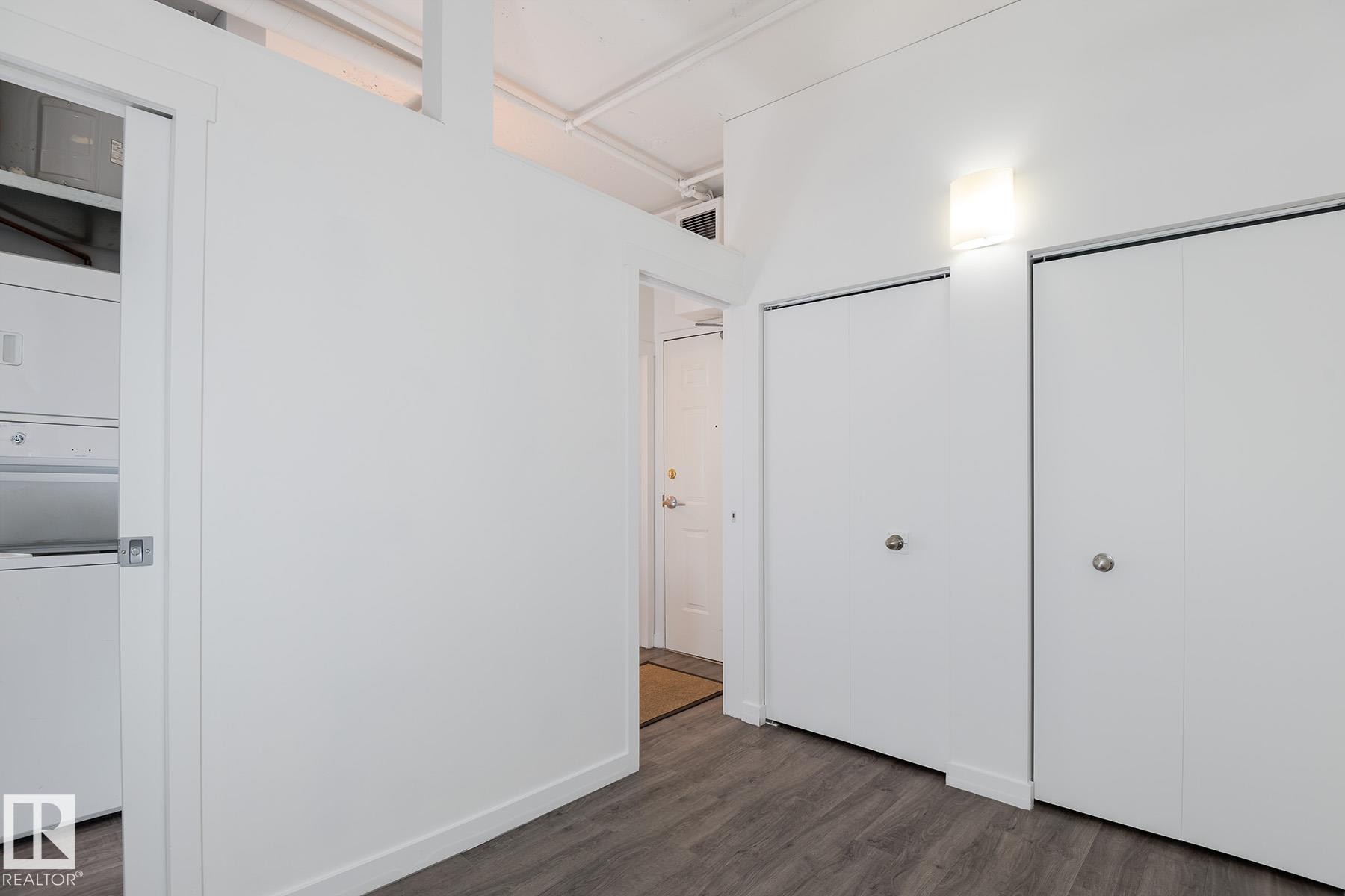 Entryway featuring two white bifold closet doors, a contemporary wall sconce, and wood-finish flooring - 910 10024 Jasper Avenue, Edmonton, AB