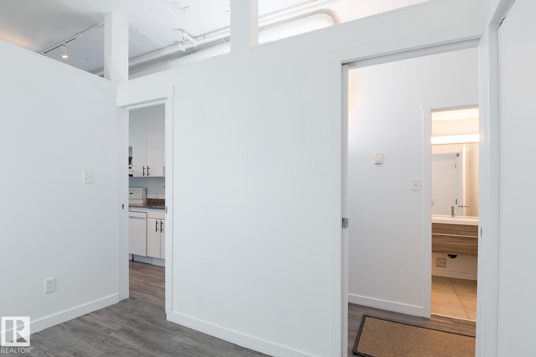 Bright interior space featuring wood-finish flooring, white walls, and exposed ceiling ductwork - 910 10024 Jasper Avenue, Edmonton, AB