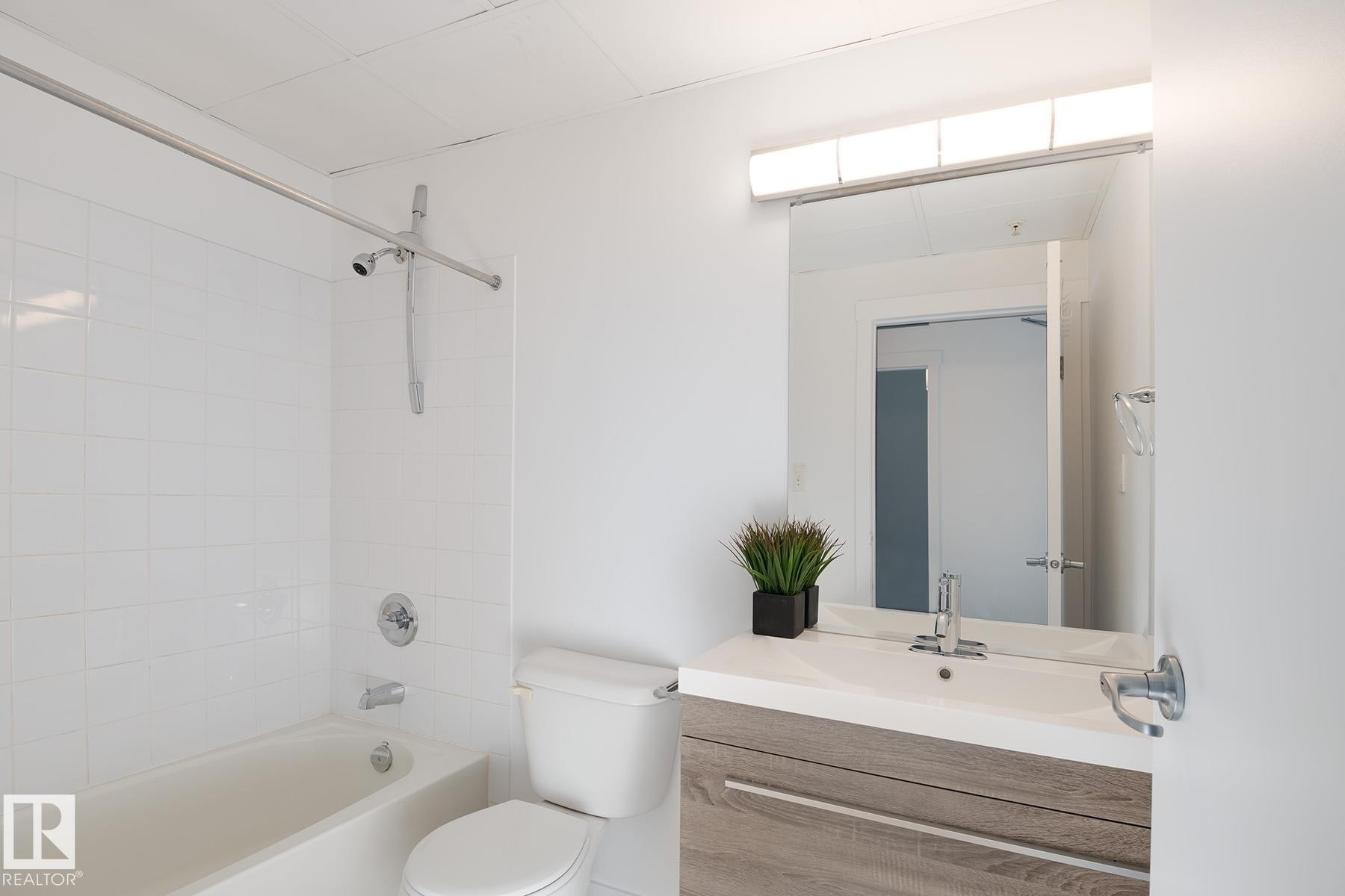 Bathroom featuring a wood-finish vanity with an integrated sink, a rectangular wall-mounted mirror, and a tub-shower combination with white subway tile surround and chrome fixtures - 910 10024 Jasper Avenue, Edmonton, AB