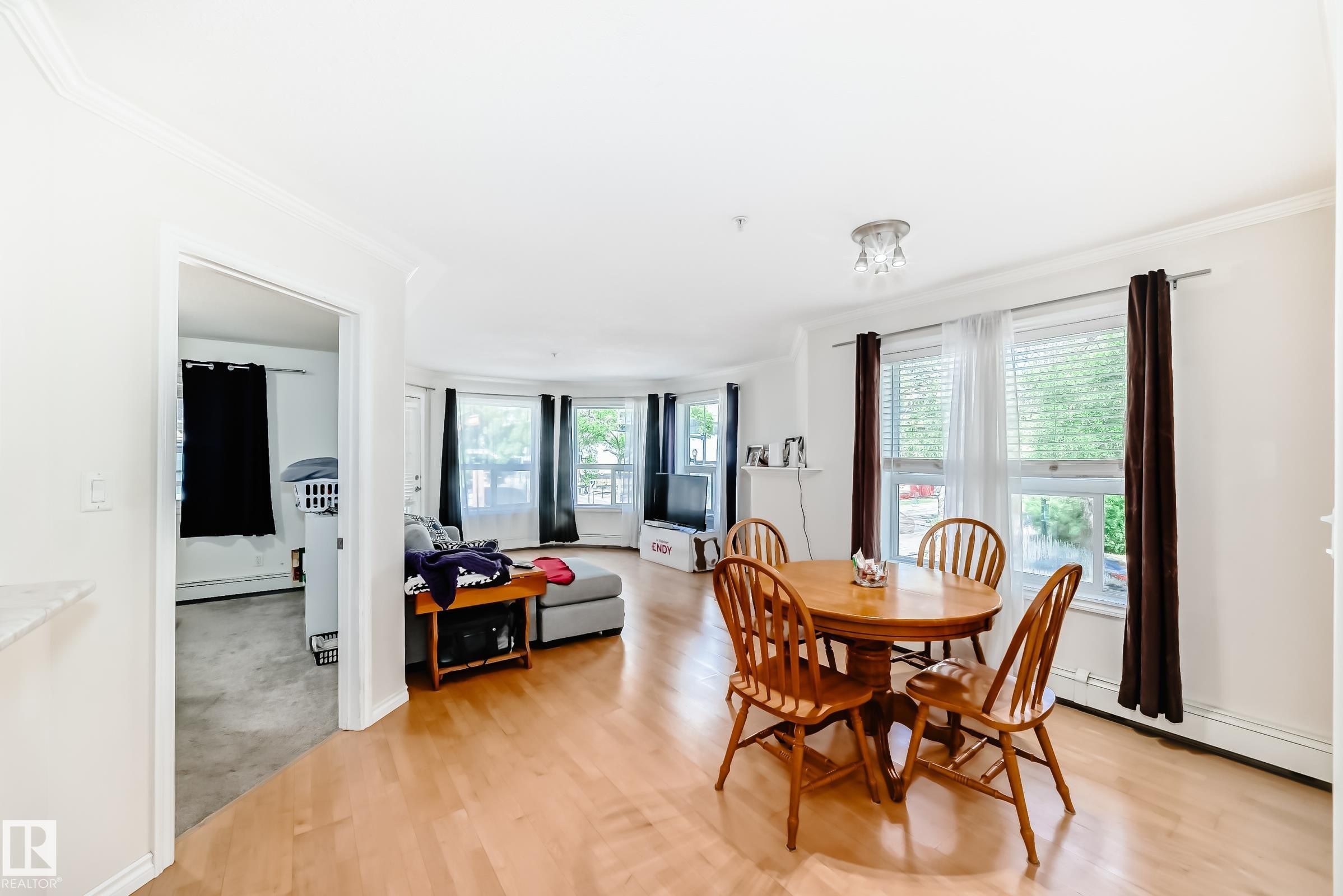Open-concept living space featuring wood-finish flooring, white walls, and bright natural light from multiple windows - 214 9938 104 Street, Edmonton, AB