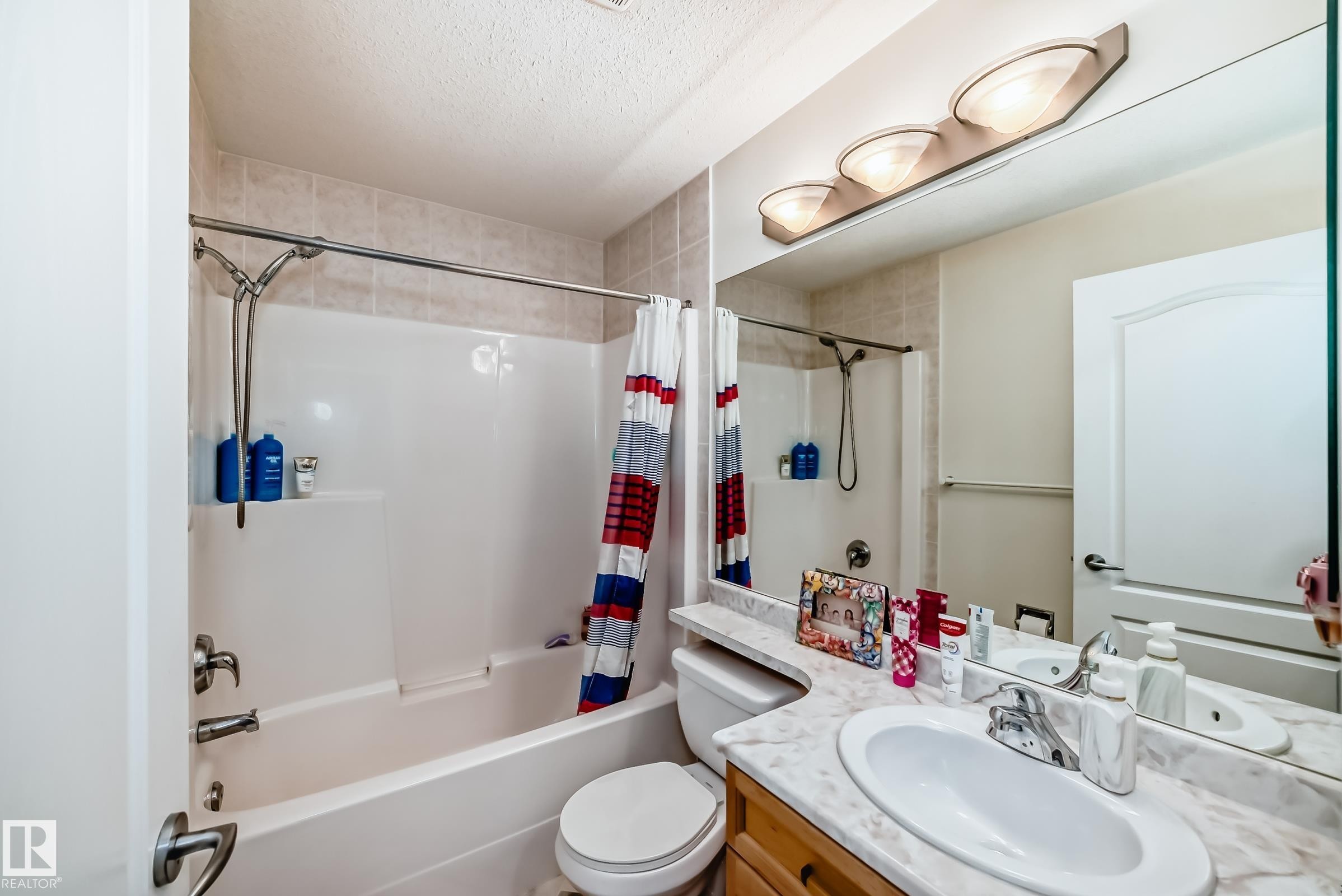 Full bathroom featuring a single vanity with a white oval sink, marble-finish countertop, and wood-finish cabinetry - 214 9938 104 Street, Edmonton, AB