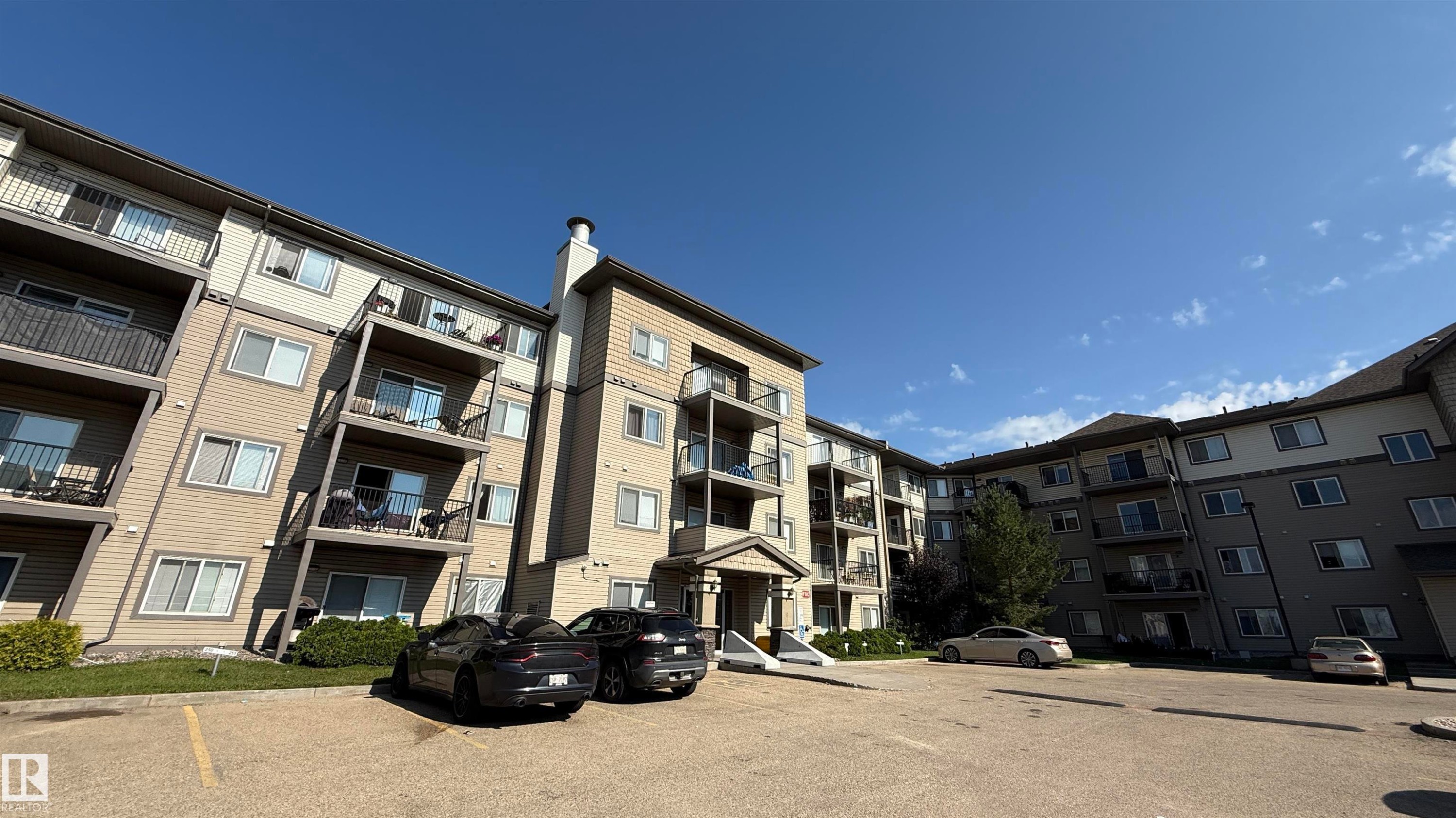 Multi-story residential building featuring balconies with dark railings, a light-colored exterior with darker trim, and a prominent entrance canopy - 133 301 Clareview Station Drive, Edmonton, AB