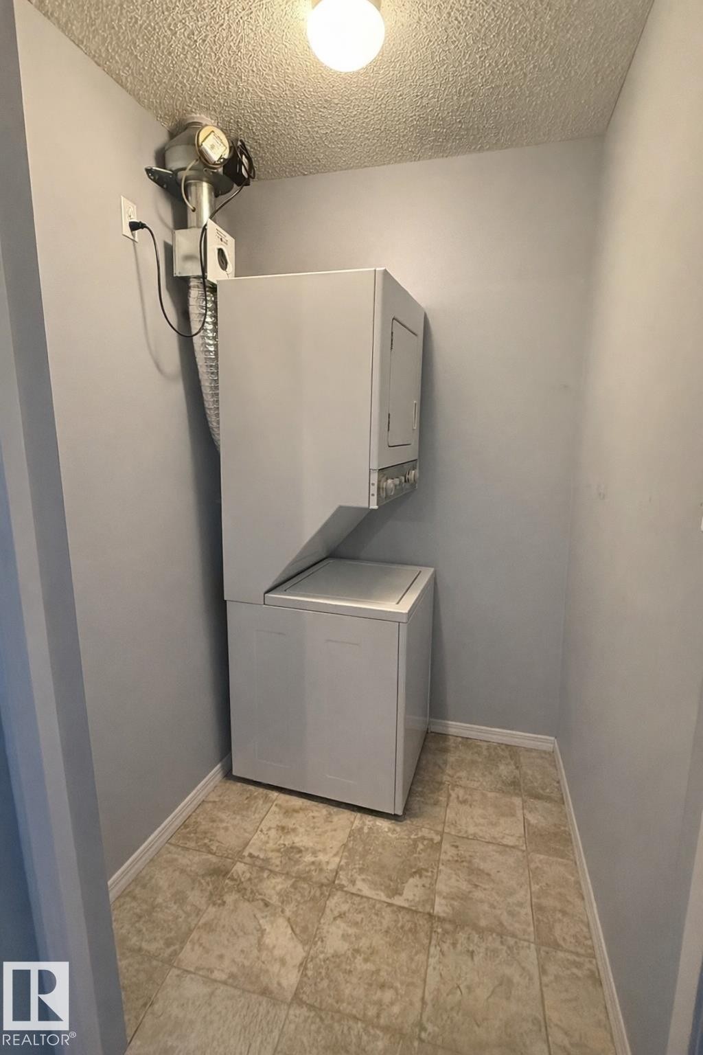 Dedicated laundry area featuring a stacked washer and dryer unit, neutral wall paint, and square floor tiles - 133 301 Clareview Station Drive, Edmonton, AB