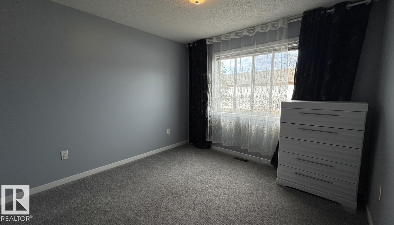 Carpeted room with a ceiling-mounted light fixture and a window featuring white trim - 133 301 Clareview Station Drive, Edmonton, AB