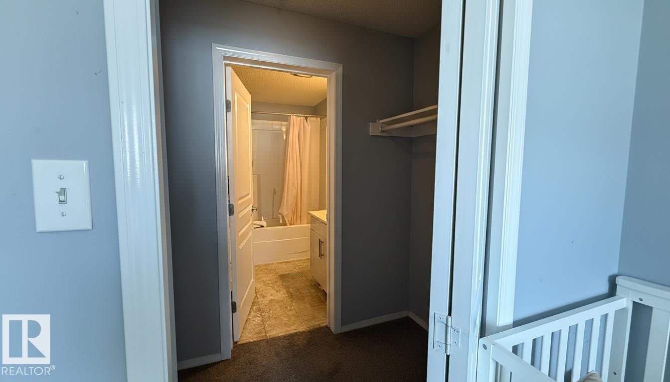 Bathroom entrance featuring a white vanity with integrated sink, a white bathtub with shower, and light-toned tile flooring - 133 301 Clareview Station Drive, Edmonton, AB
