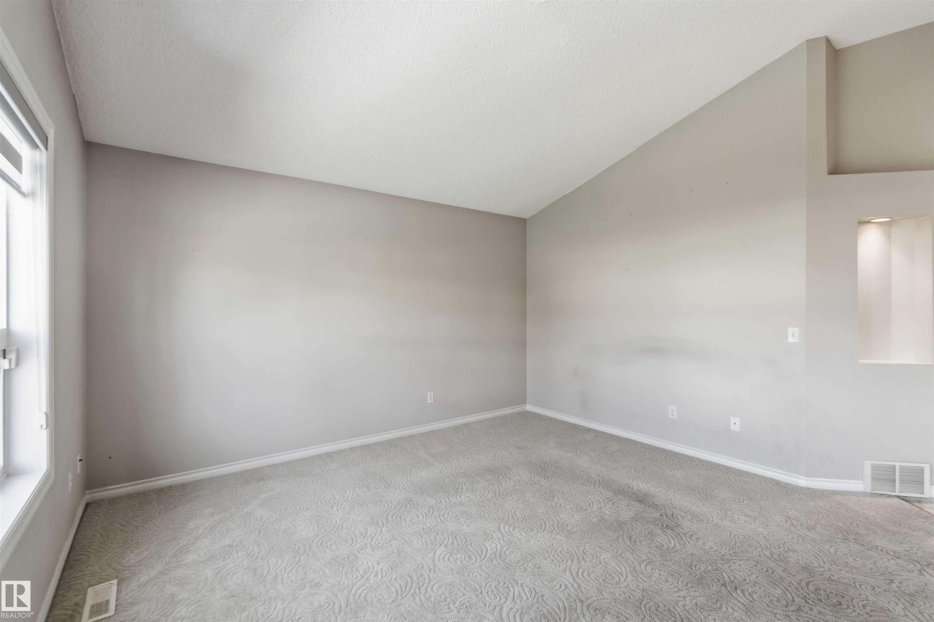 Room featuring a vaulted ceiling, neutral wall paint, and patterned gray carpeting - 2012 35A Avenue, Edmonton, AB