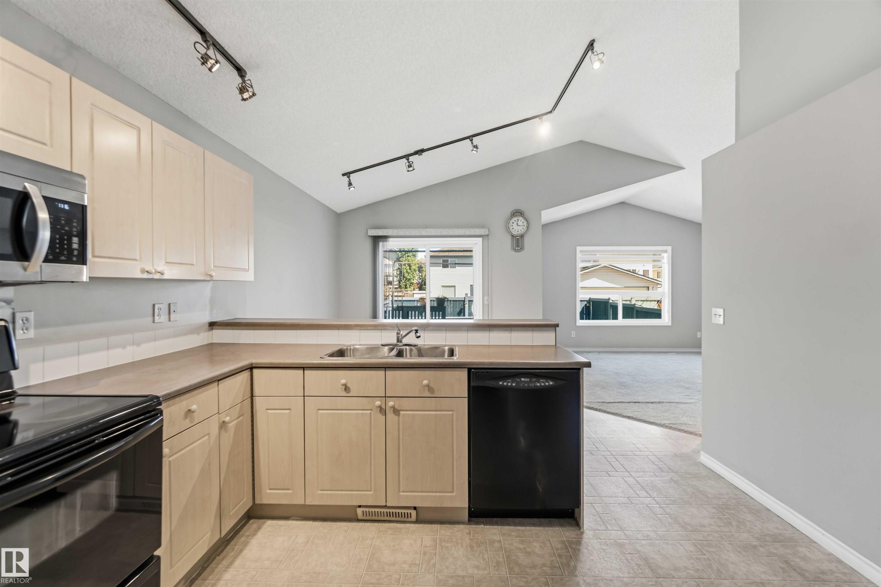 Kitchen featuring light wood-finish cabinetry, stainless steel microwave, black electric range, and black dishwasher - 2012 35A Avenue, Edmonton, AB
