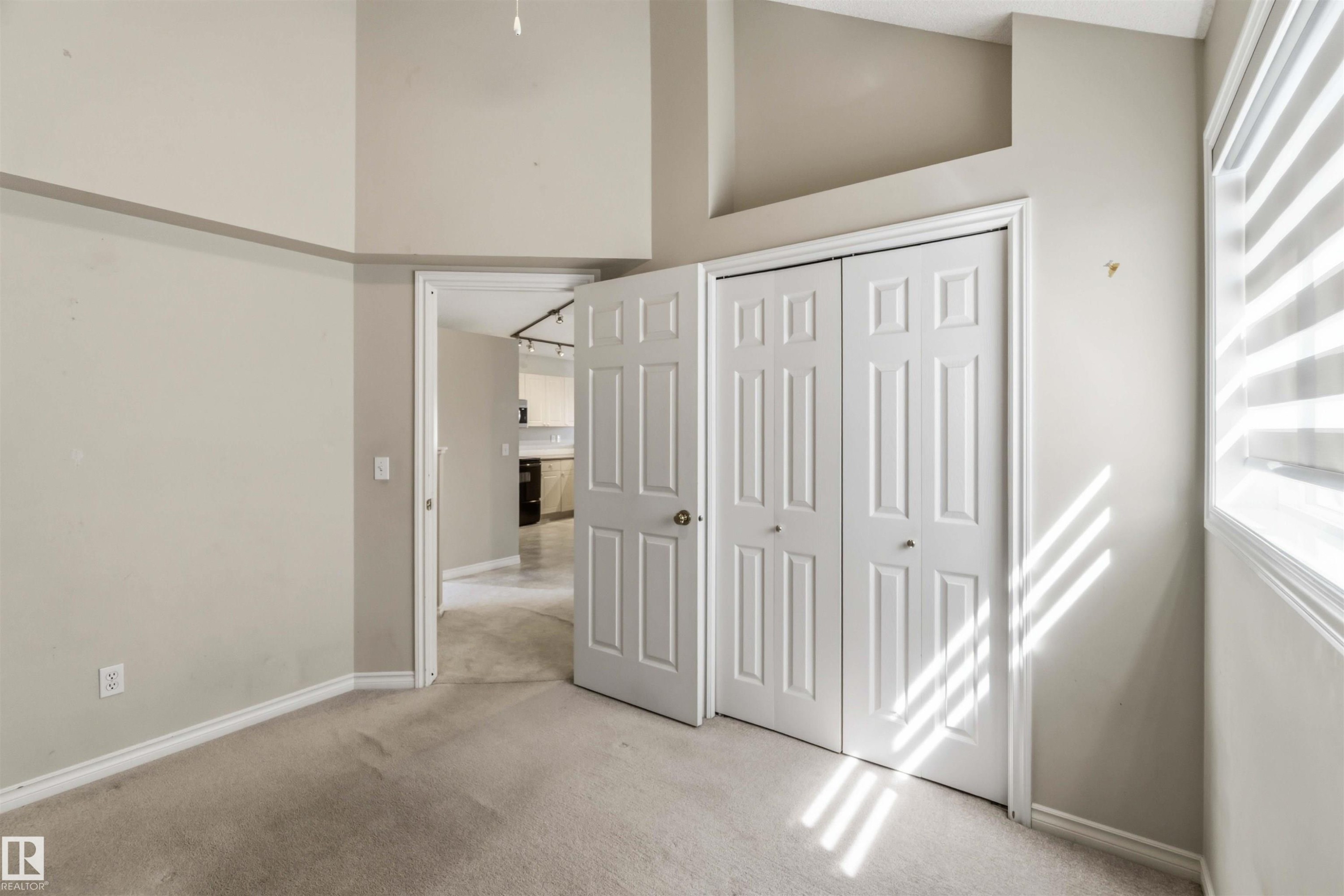 Carpeted interior space with a bi-fold closet door, neutral wall tones, and a window with horizontal blinds - 2012 35A Avenue, Edmonton, AB