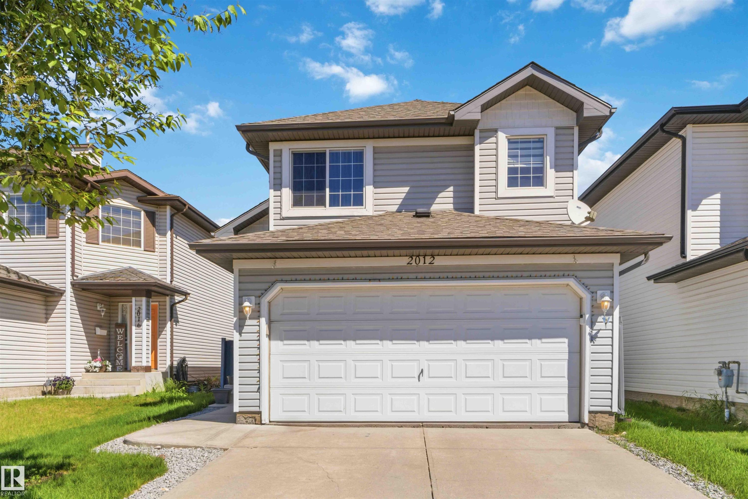 Contemporary two-story residence featuring light gray horizontal siding, a two-car garage with a panel door, brown shingle roofing, and a prominent front-facing dormer with a multi-pane window - 2012 35A Avenue, Edmonton, AB