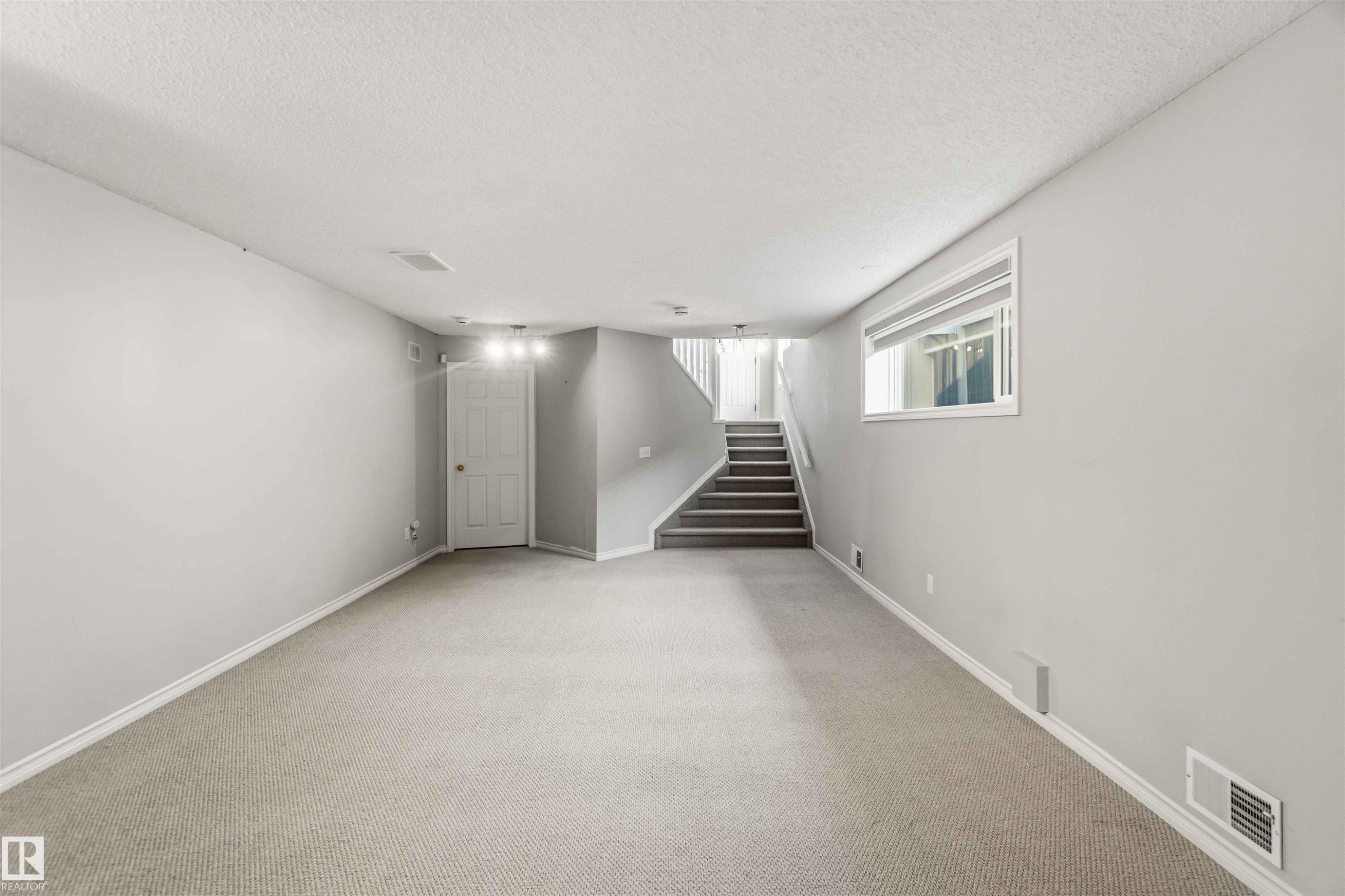 Spacious room featuring light gray carpeting, neutral wall paint, and white baseboards - 2012 35A Avenue, Edmonton, AB