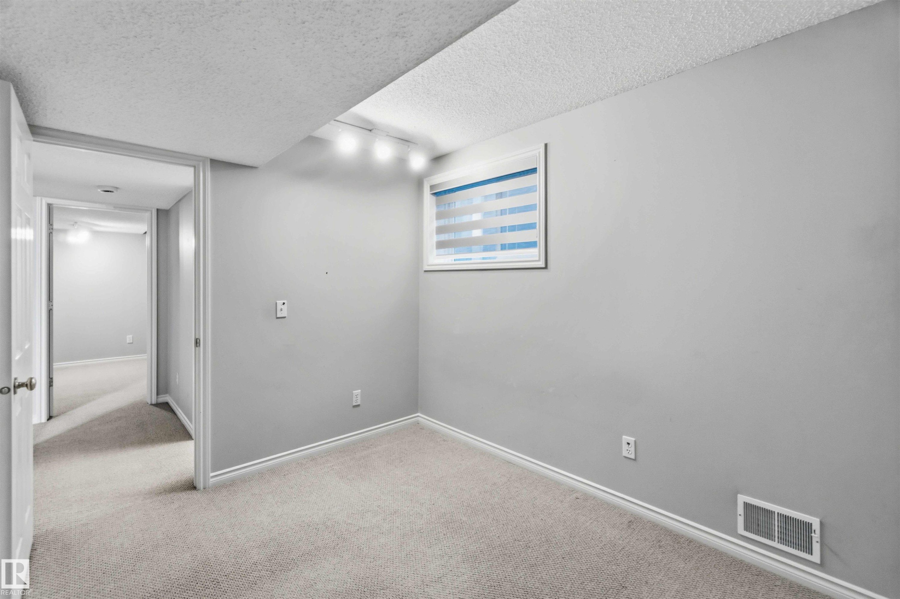 Carpeted room featuring a window with horizontal blinds, track lighting, and a baseboard vent - 2012 35A Avenue, Edmonton, AB