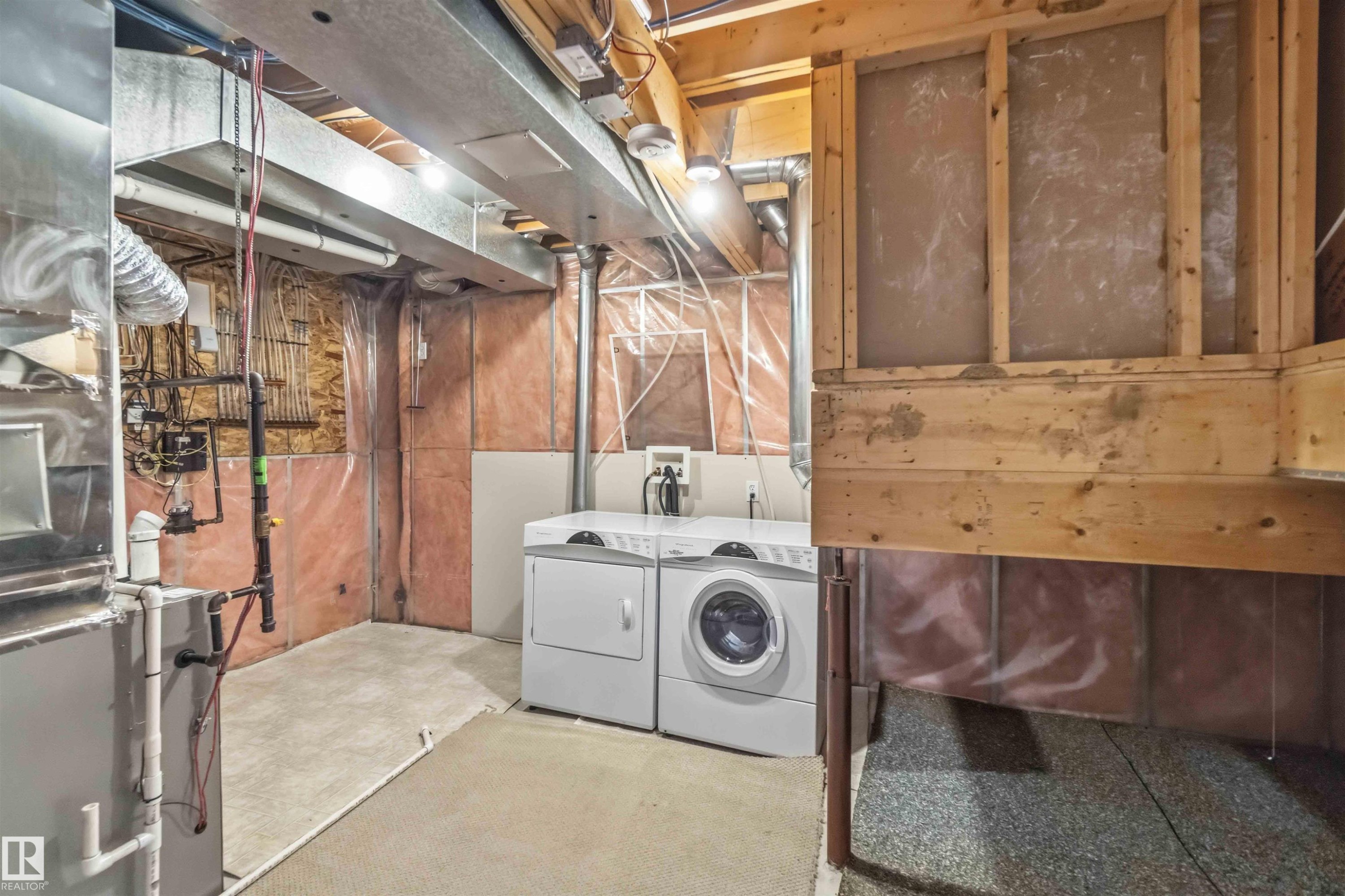 Unfinished basement space featuring a washer and dryer, exposed ceiling joists and ductwork, concrete flooring, and partial wall insulation - 2012 35A Avenue, Edmonton, AB