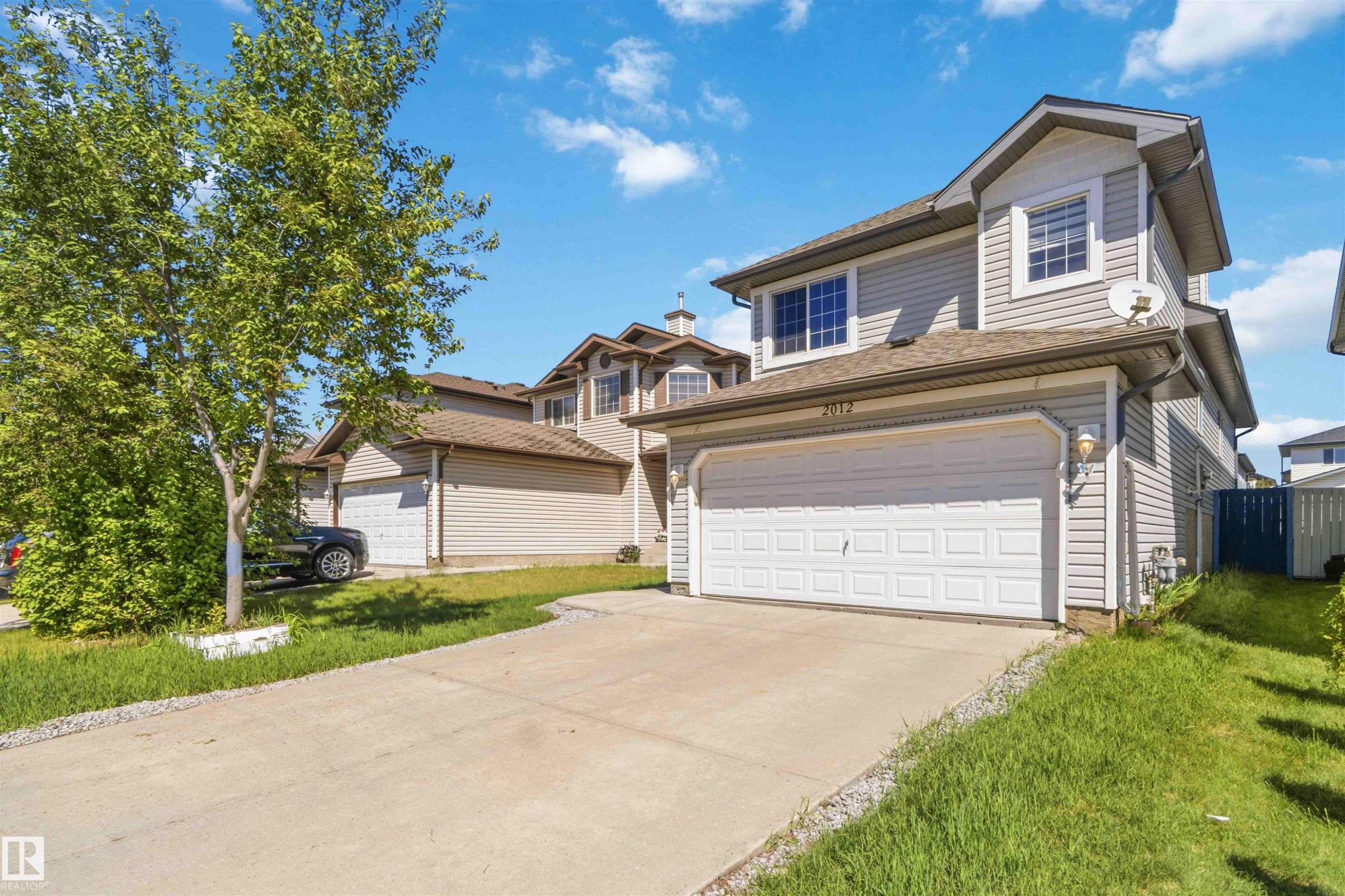 Two-story residence featuring light gray siding, an attached garage with a white panel door, a concrete driveway, and a partially fenced yard - 2012 35A Avenue, Edmonton, AB