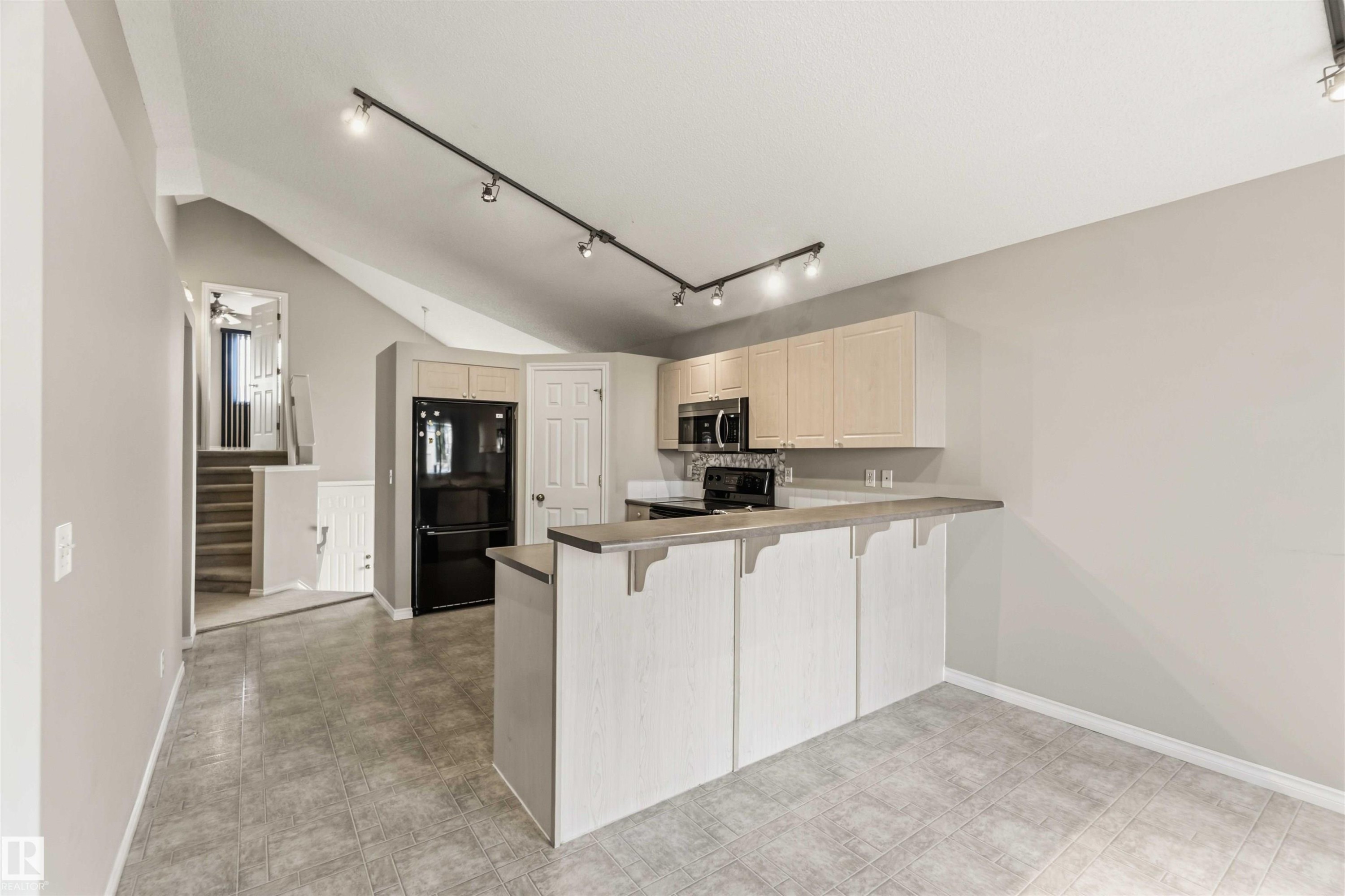Kitchen featuring black appliances, light wood-finish cabinetry, and a breakfast bar - 2012 35A Avenue, Edmonton, AB