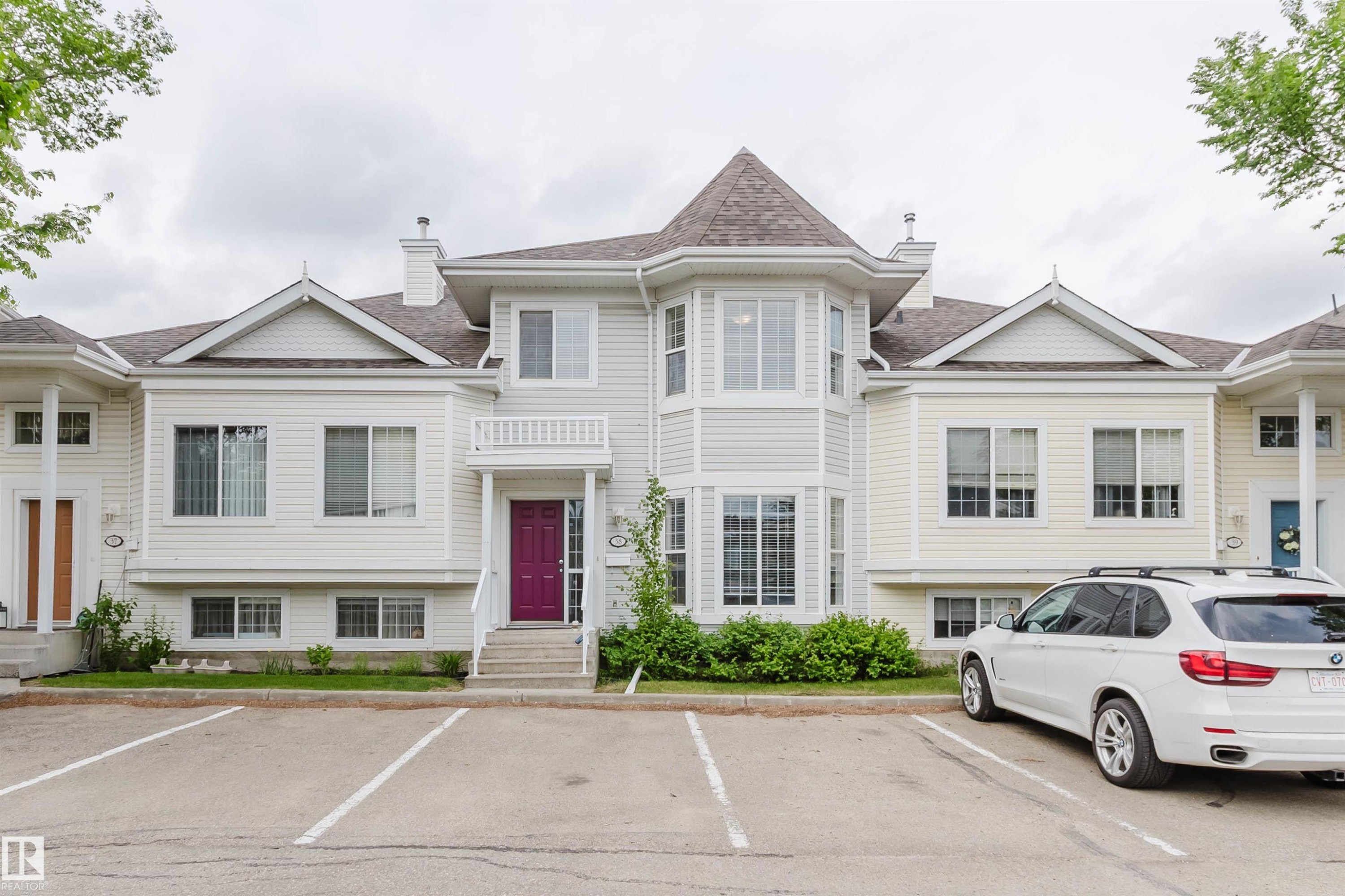 Multi-level townhouse exterior featuring light-colored siding, a prominent turret with multiple windows, and a vibrant purple entry door with white railings - 38 1780 Glastonbury Boulevard, Edmonton, AB