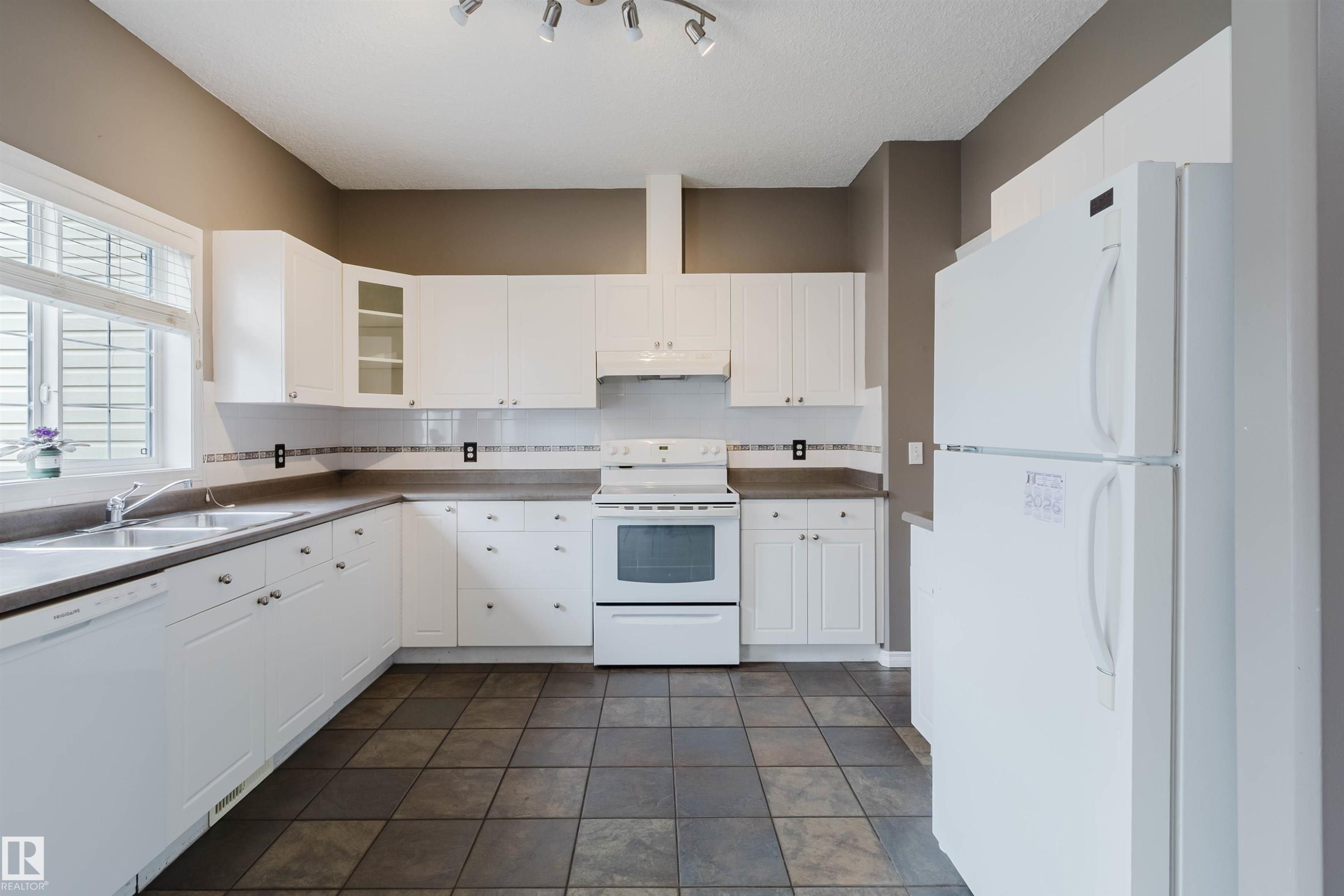 Kitchen featuring white cabinetry, a double basin stainless steel sink, a dishwasher, a white oven/range, and tile flooring - 38 1780 Glastonbury Boulevard, Edmonton, AB