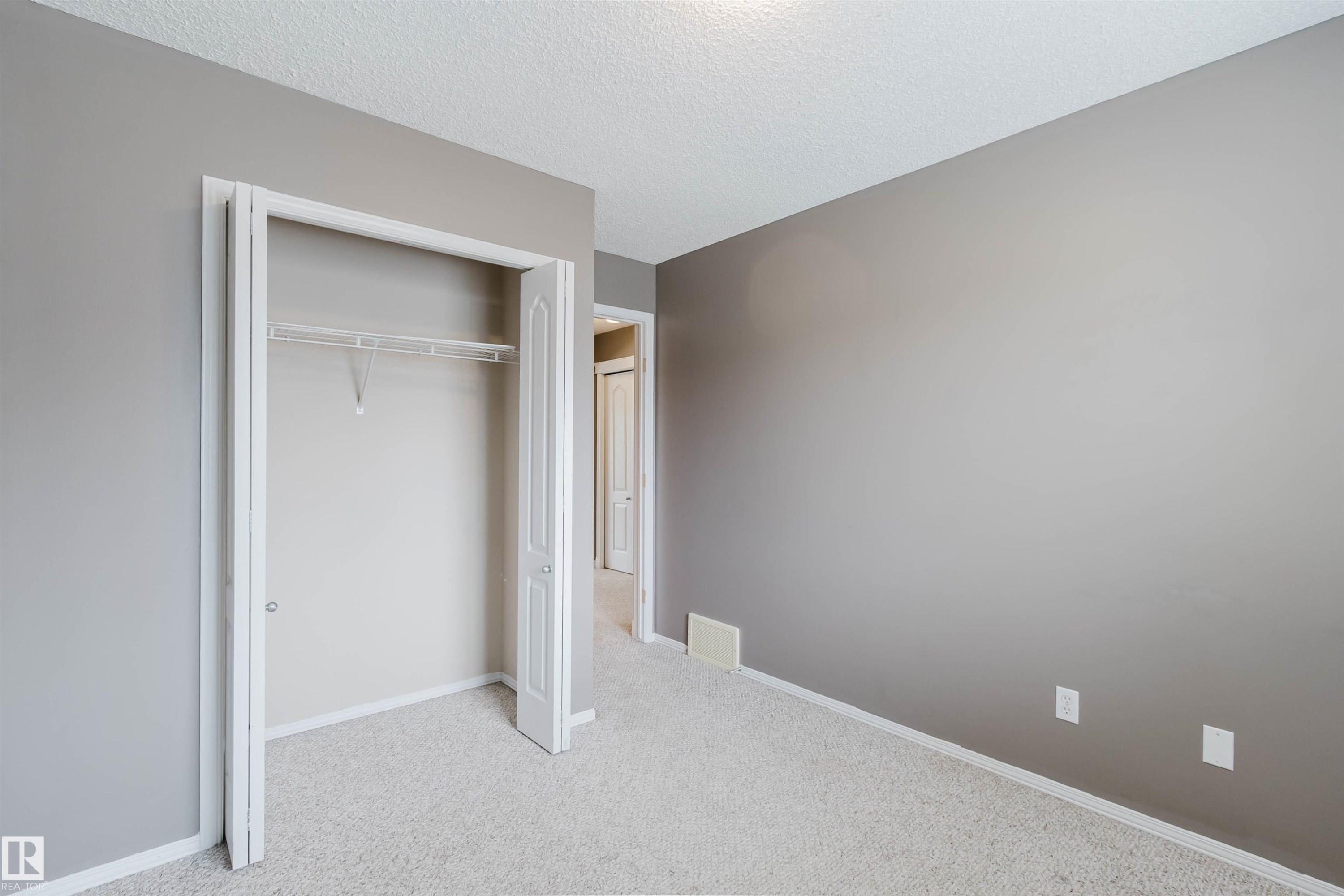 Carpeted room with a bi-fold door closet featuring a wire shelf and hanging rod - 38 1780 Glastonbury Boulevard, Edmonton, AB