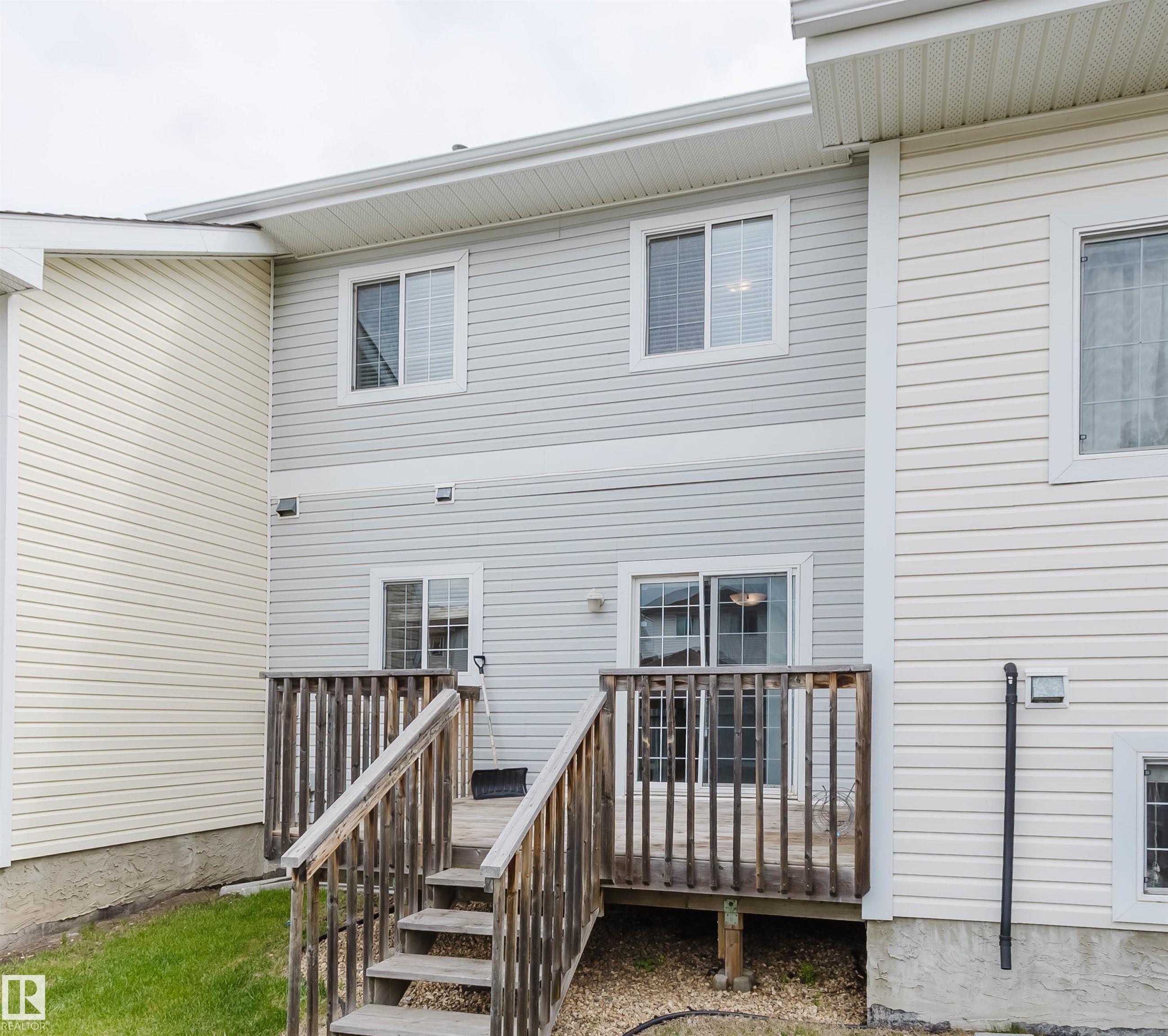 Rear exterior featuring a multi-level wood deck with stairs to ground level, light-colored horizontal siding, and multiple windows - 38 1780 Glastonbury Boulevard, Edmonton, AB