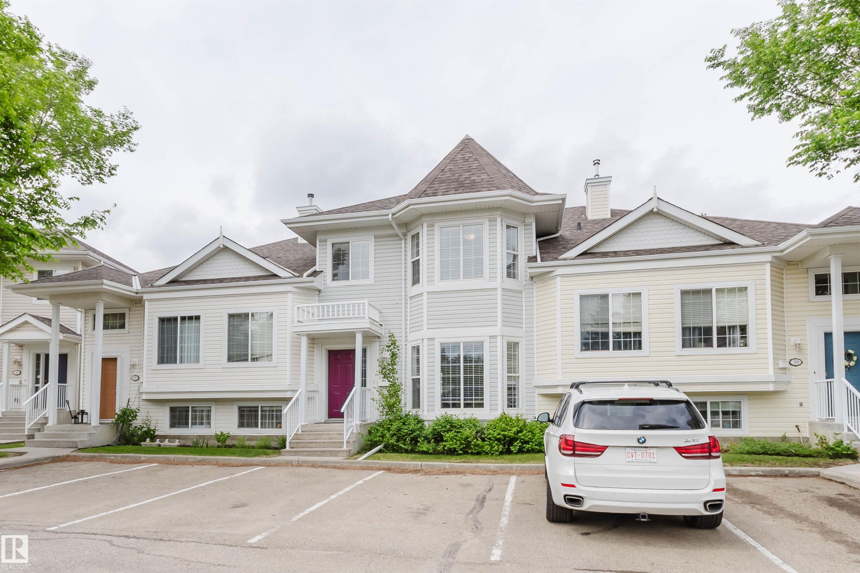 Multi-level townhome exterior featuring light-colored siding, a prominent turret-style window feature, multiple gables, and a pitched roof - 38 1780 Glastonbury Boulevard, Edmonton, AB