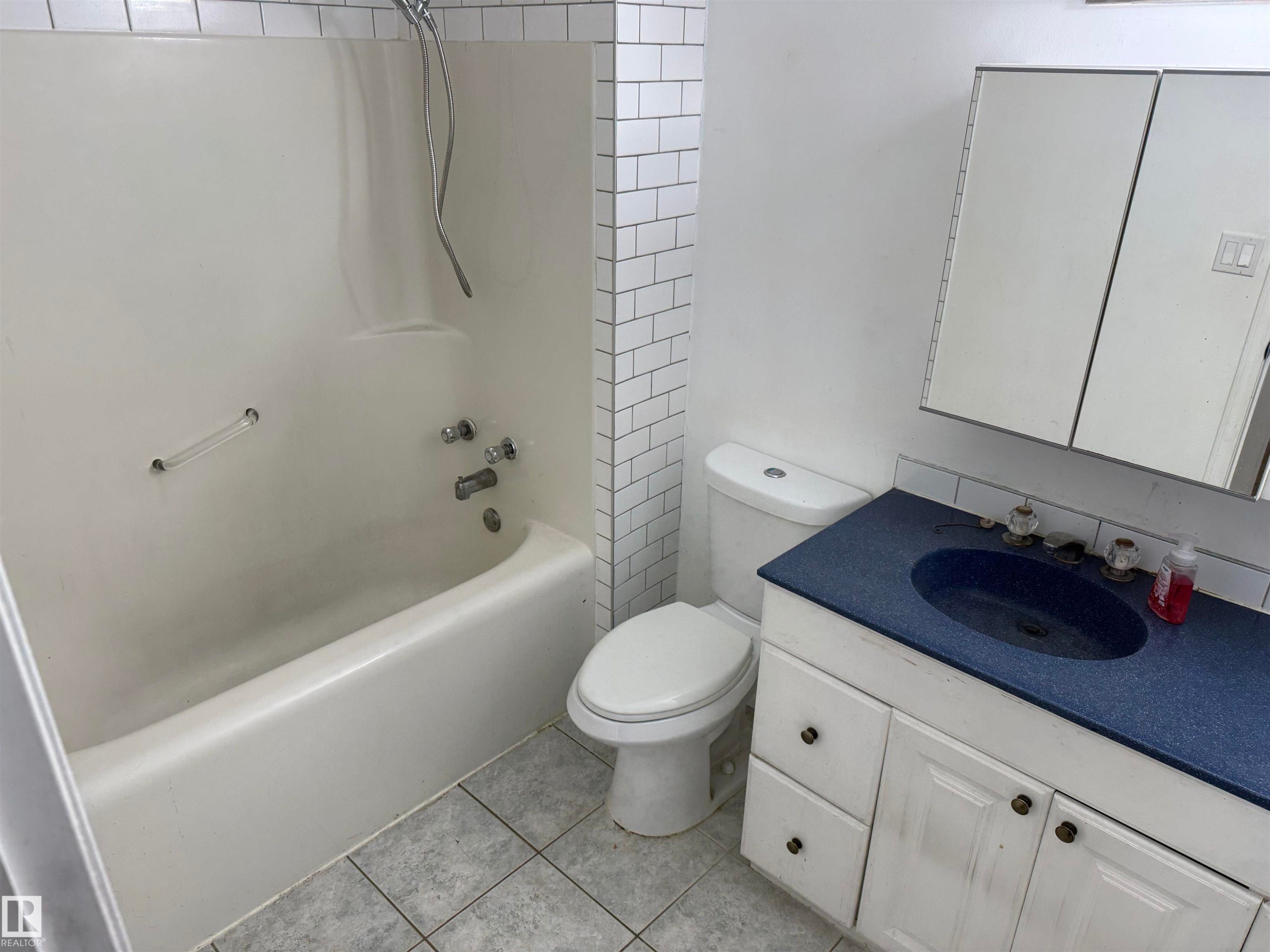 Bathroom featuring a white tub-shower combination, subway tile surround, white toilet, and a vanity with a blue countertop and white cabinetry - 14537 121 Street, Edmonton, AB