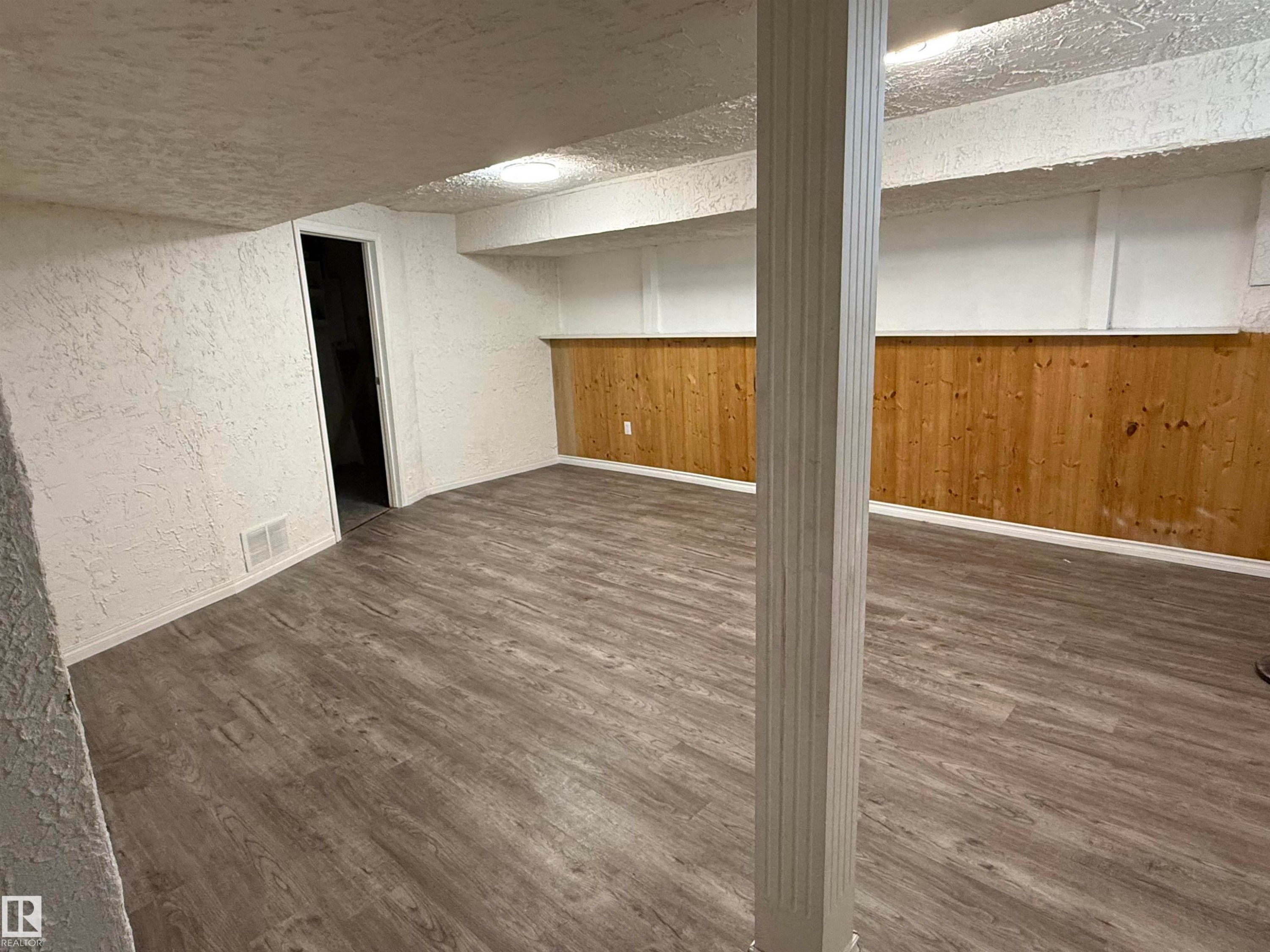 Spacious room featuring wood-finish flooring, white textured walls, and natural wood paneling - 14537 121 Street, Edmonton, AB