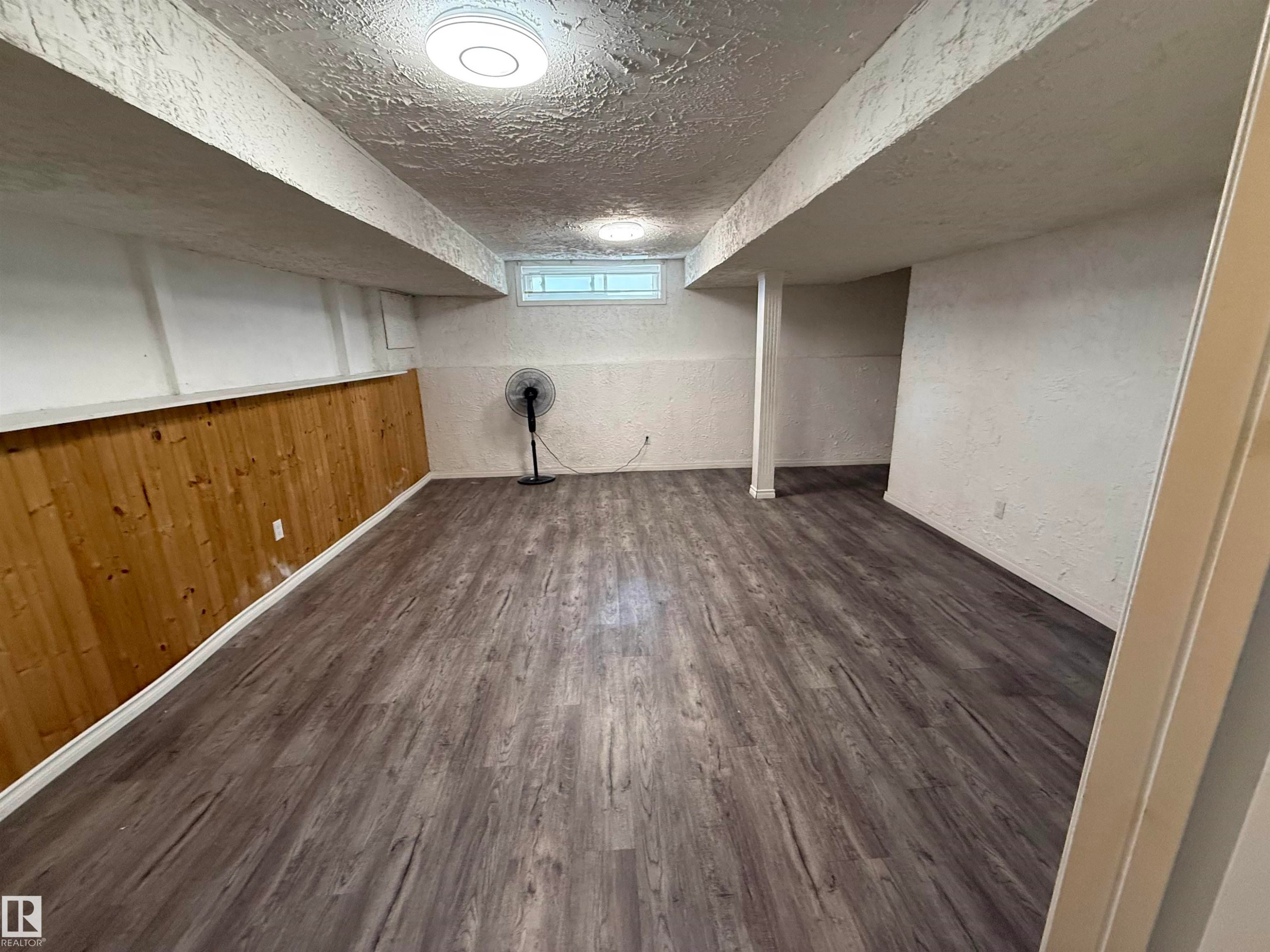 Spacious area featuring wood-finish flooring, half-wall wood paneling, and a single window - 14537 121 Street, Edmonton, AB