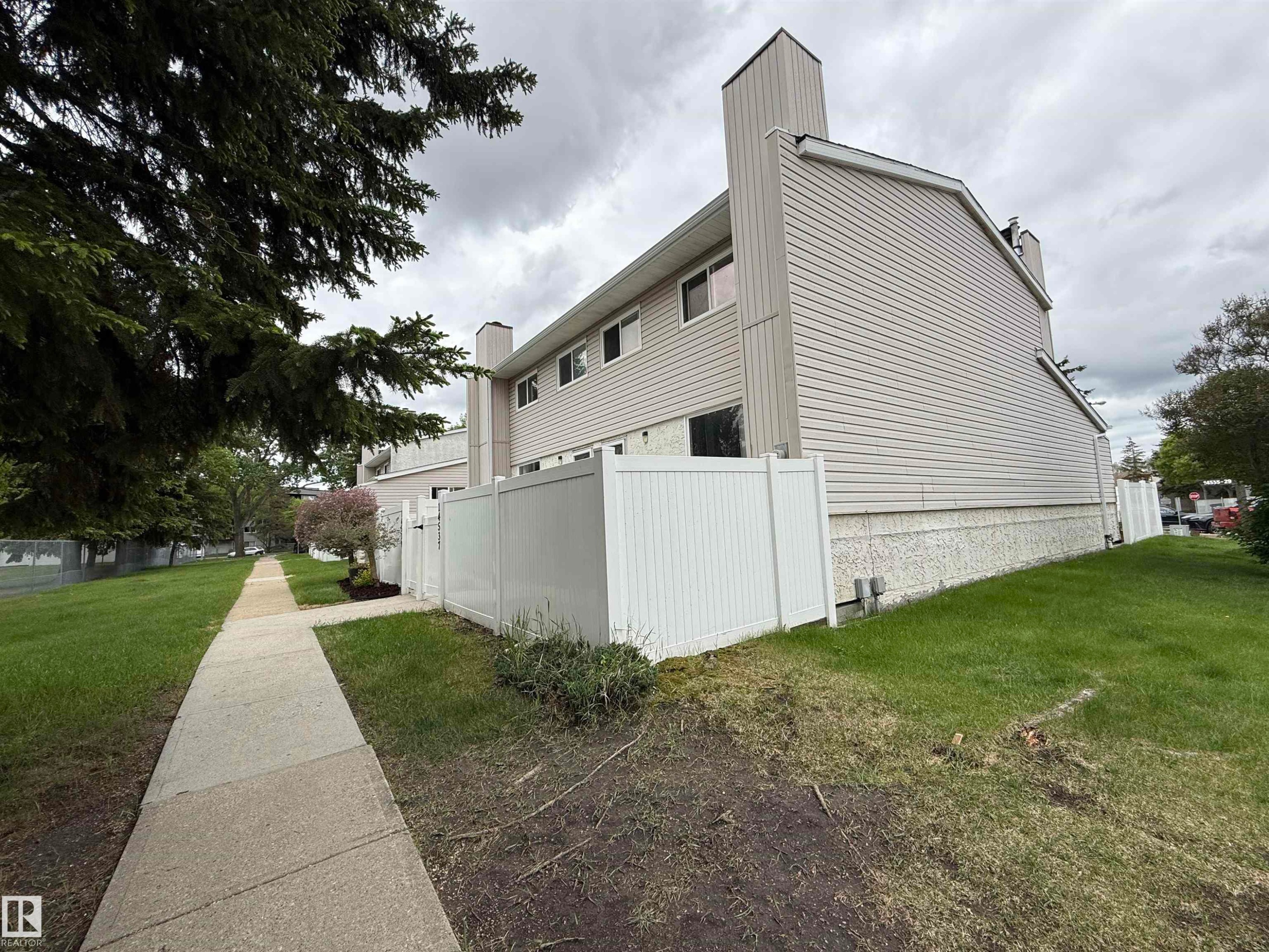Townhome exterior featuring light-colored siding, a white privacy fence, and a concrete sidewalk - 14537 121 Street, Edmonton, AB