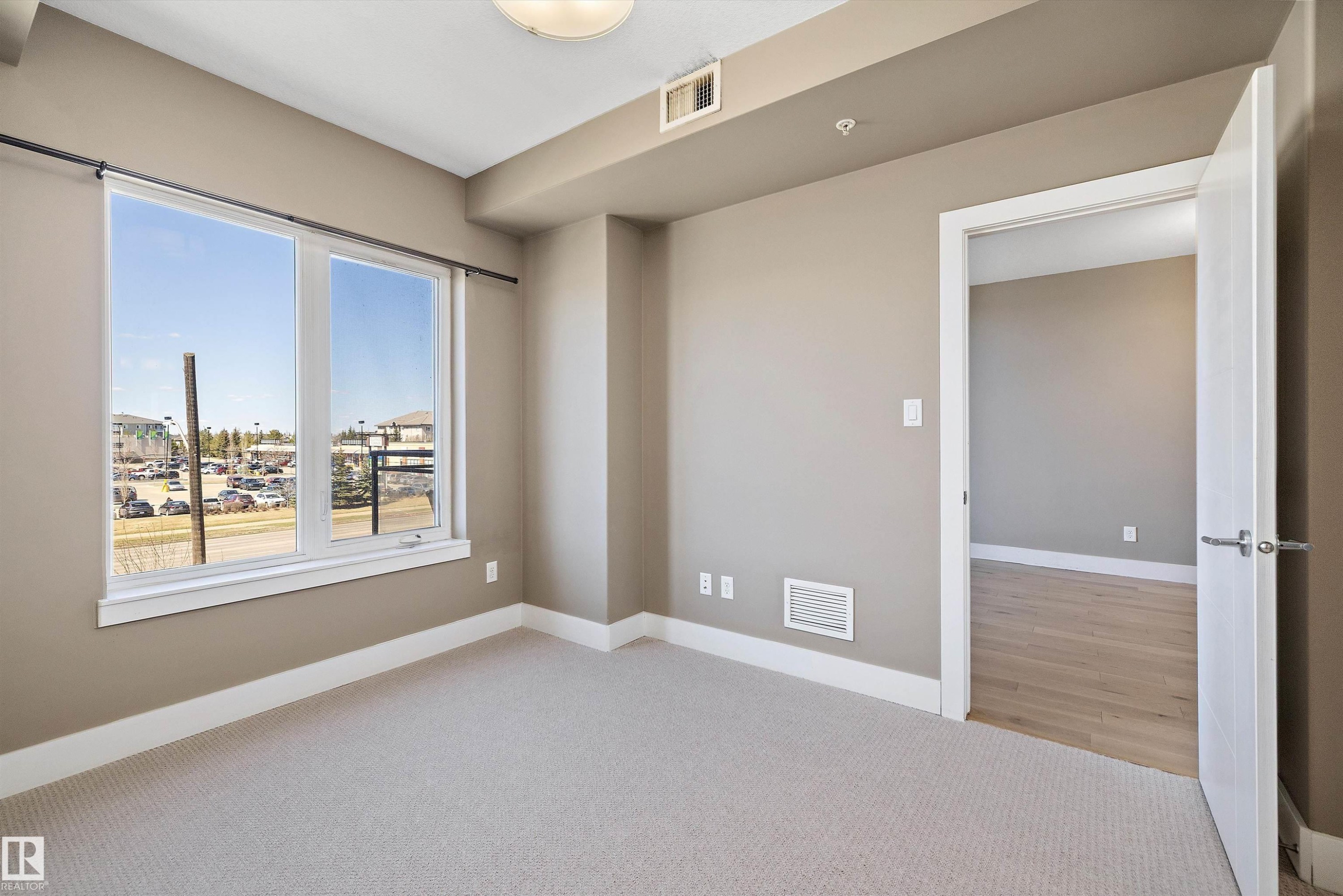 Bright interior space featuring a large window, neutral carpeting, and a white interior door - 307 11080 Ellerslie Rd Sw, Edmonton, AB