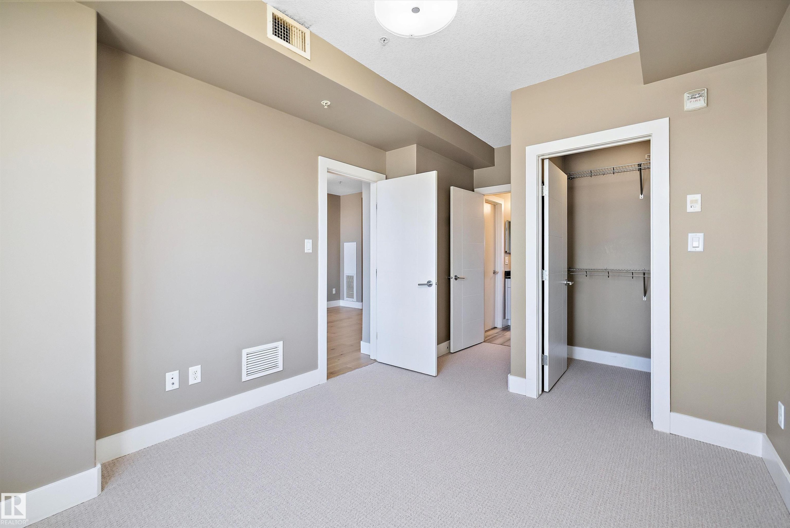 Spacious interior room featuring light beige wall paint, white trim, and light-colored carpeting - 307 11080 Ellerslie Rd Sw, Edmonton, AB