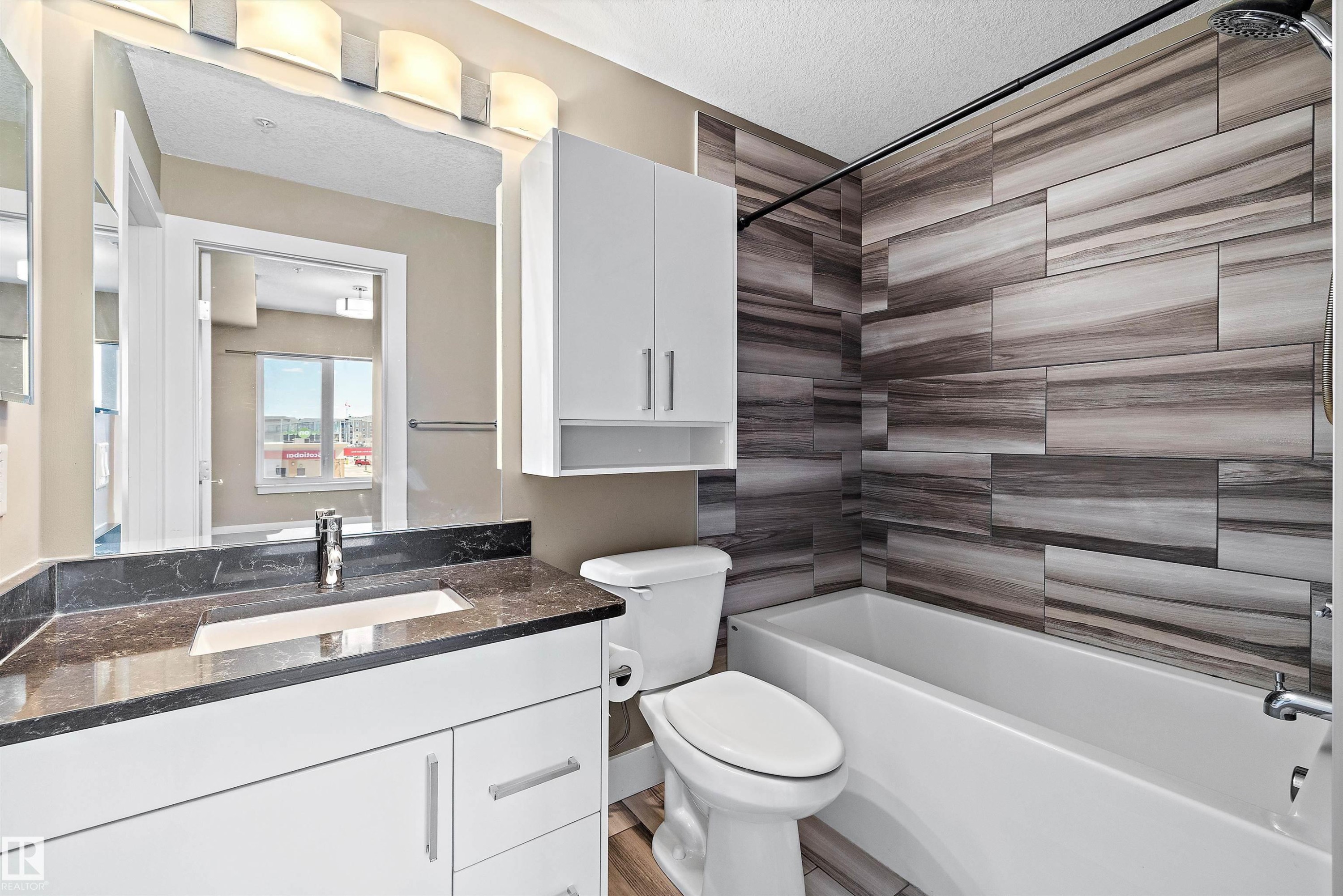 Modern bathroom featuring a white vanity with dark stone-finish countertop, undermount sink, and chrome faucet - 307 11080 Ellerslie Rd Sw, Edmonton, AB