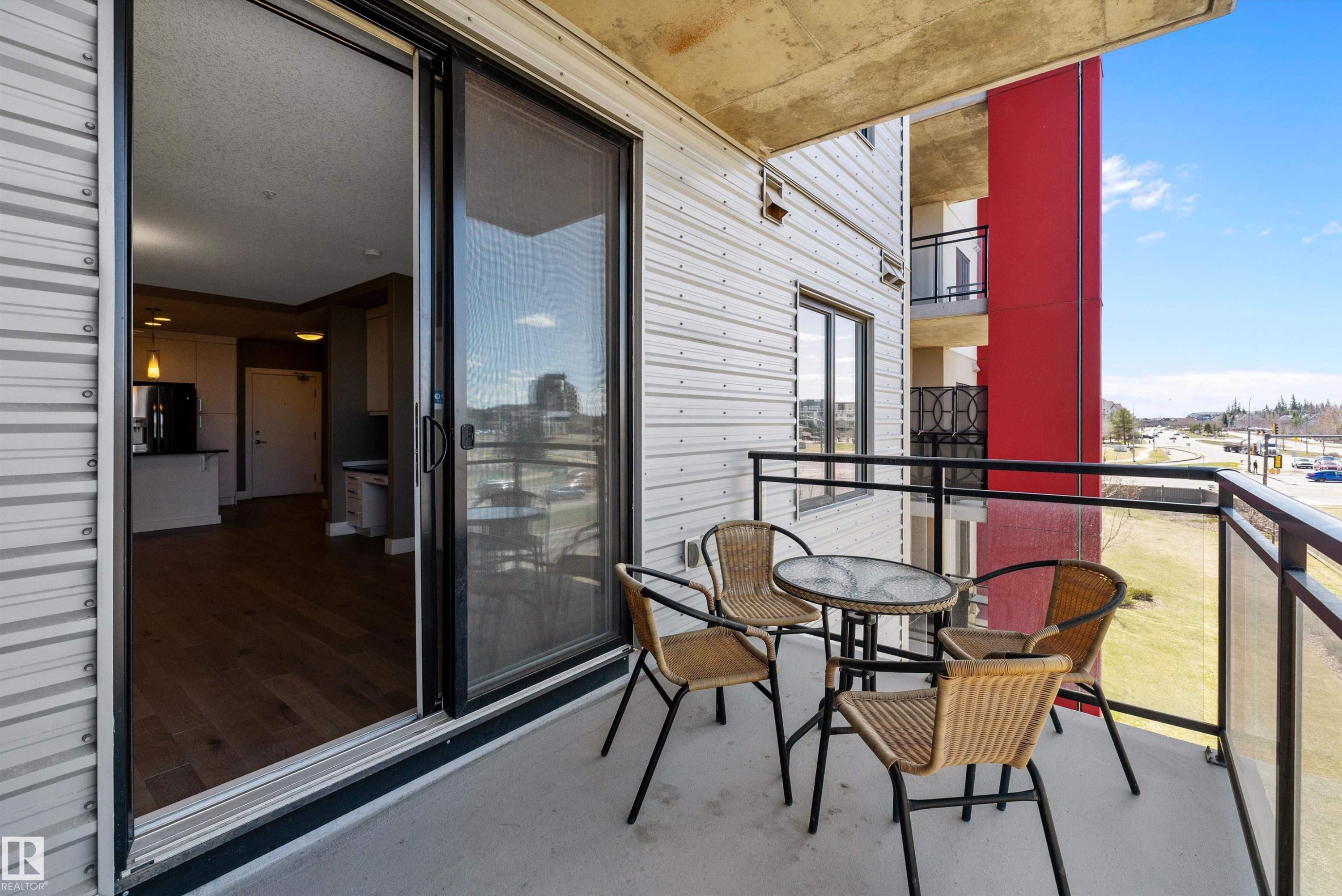 Private west facing balcony featuring concrete flooring and a glass panel railing system with black metal supports. - 307 11080 Ellerslie Rd Sw, Edmonton, AB