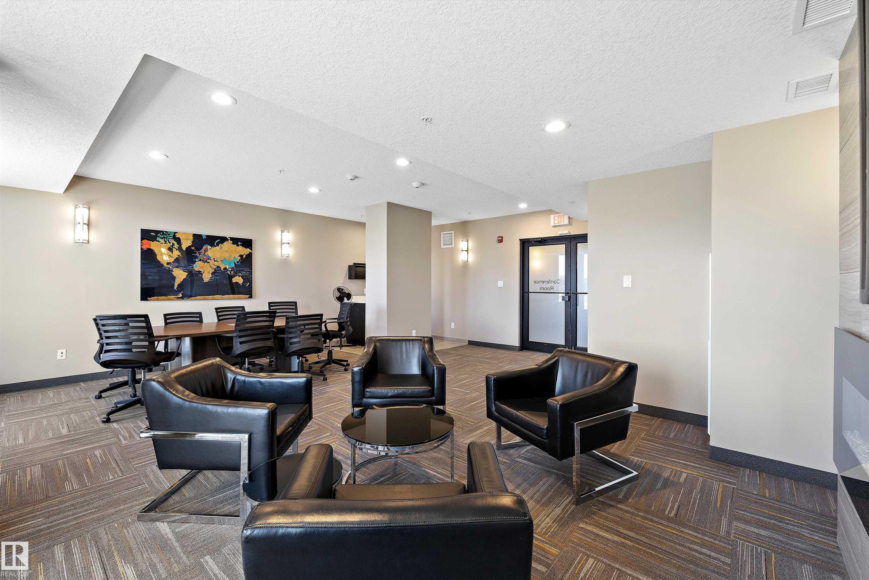 Multifunctional office common area featuring a wood-finish conference table, contemporary linear fireplace with a textured surround, recessed lighting, wall sconces, and patterned carpet flooring. - 307 11080 Ellerslie Rd Sw, Edmonton, AB