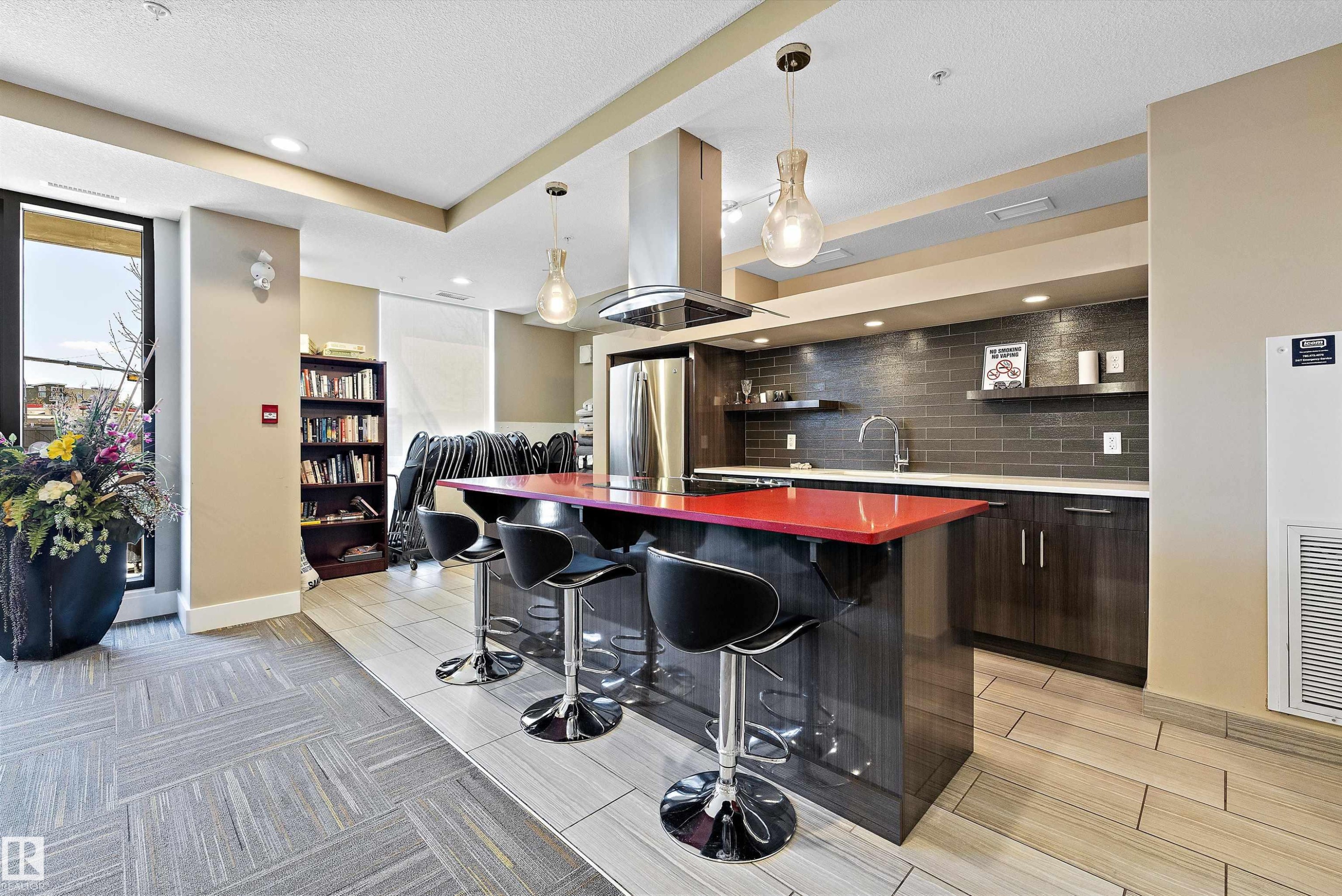The Recreation Room has a modern kitchen featuring a striking red island countertop, stainless steel appliances, dark wood-finish cabinetry, and a dark subway tile backsplash, with a pool table and a lounge type seating to enjoy with your company. - 307 11080 Ellerslie Rd Sw, Edmonton, AB